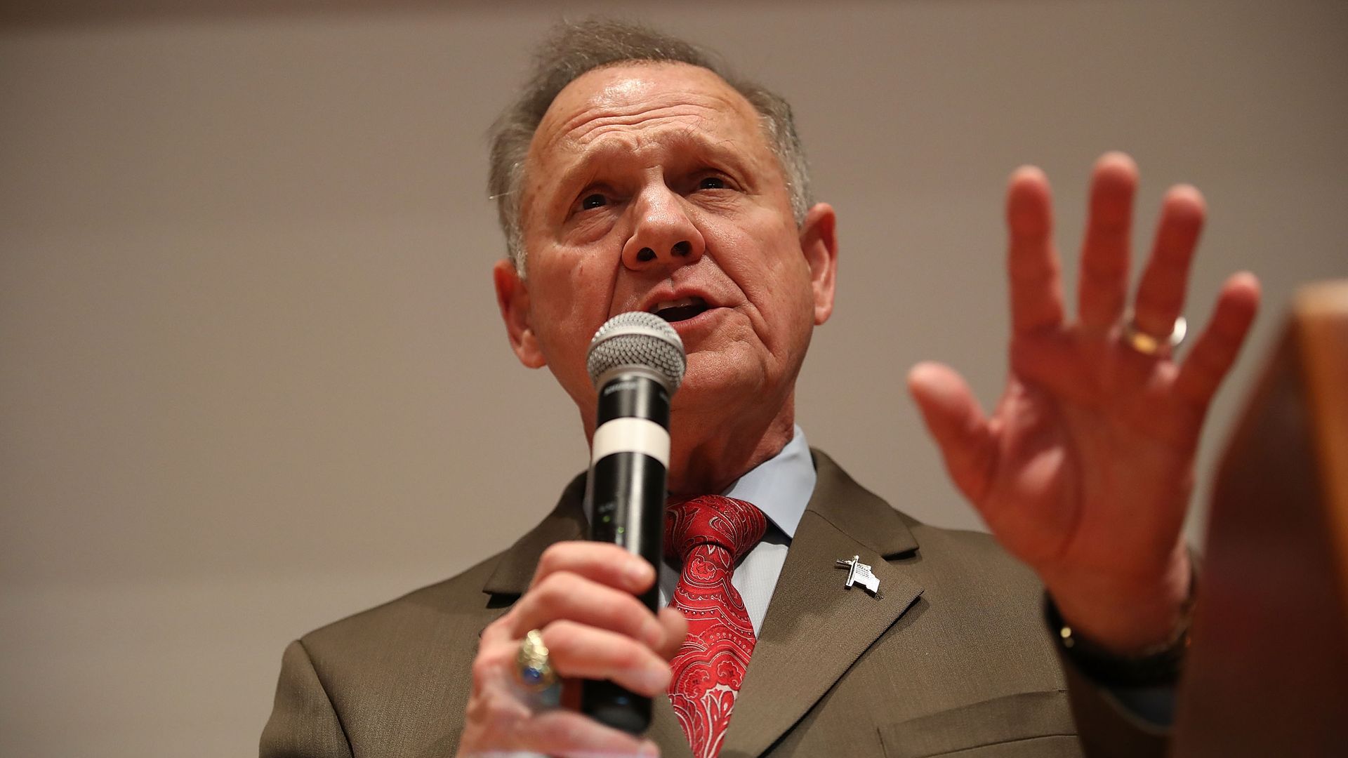 In this image, Roy Moore speaks into a microphone and waves a hand.