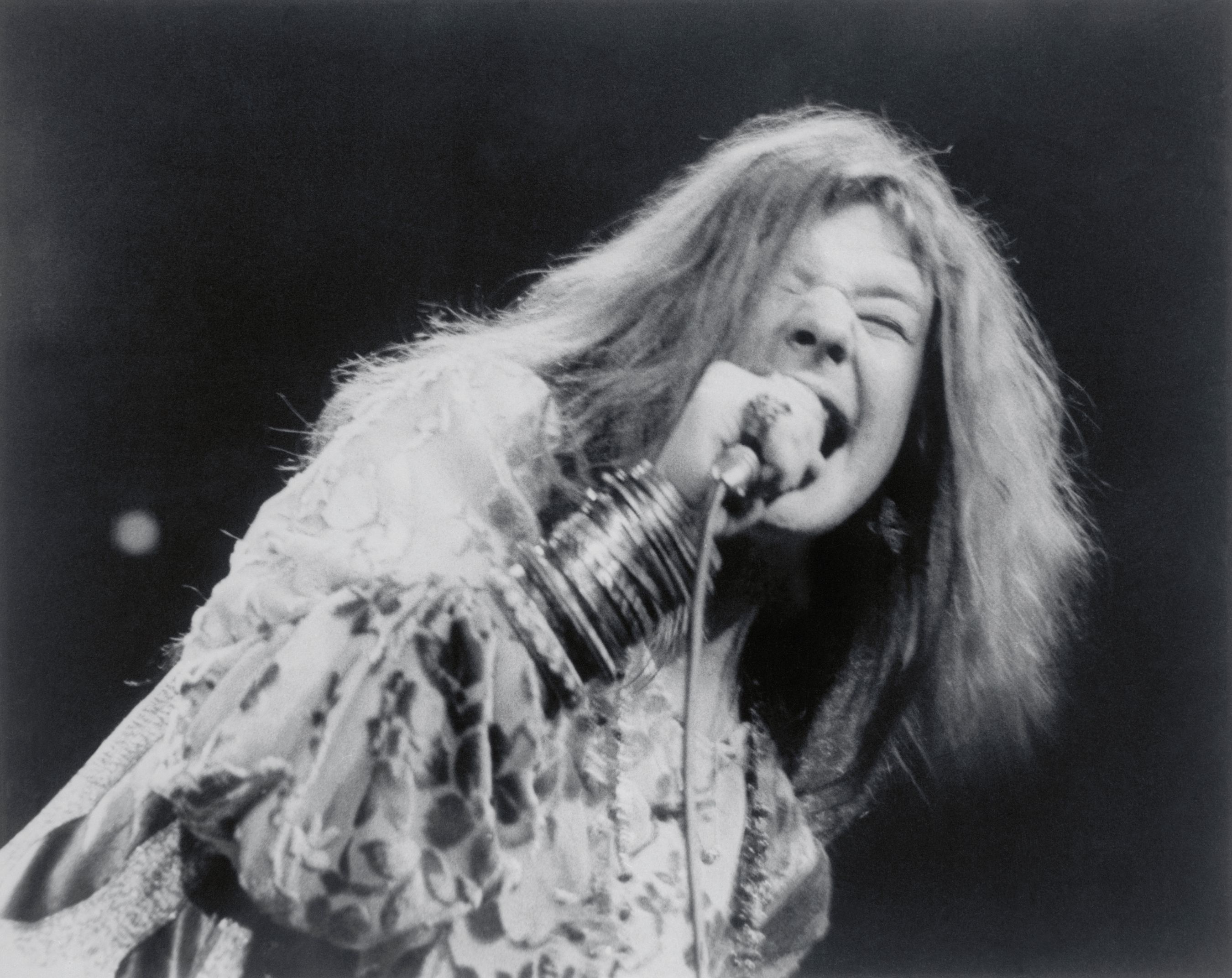 Janis Joplin performs on stage in black and white photo.
