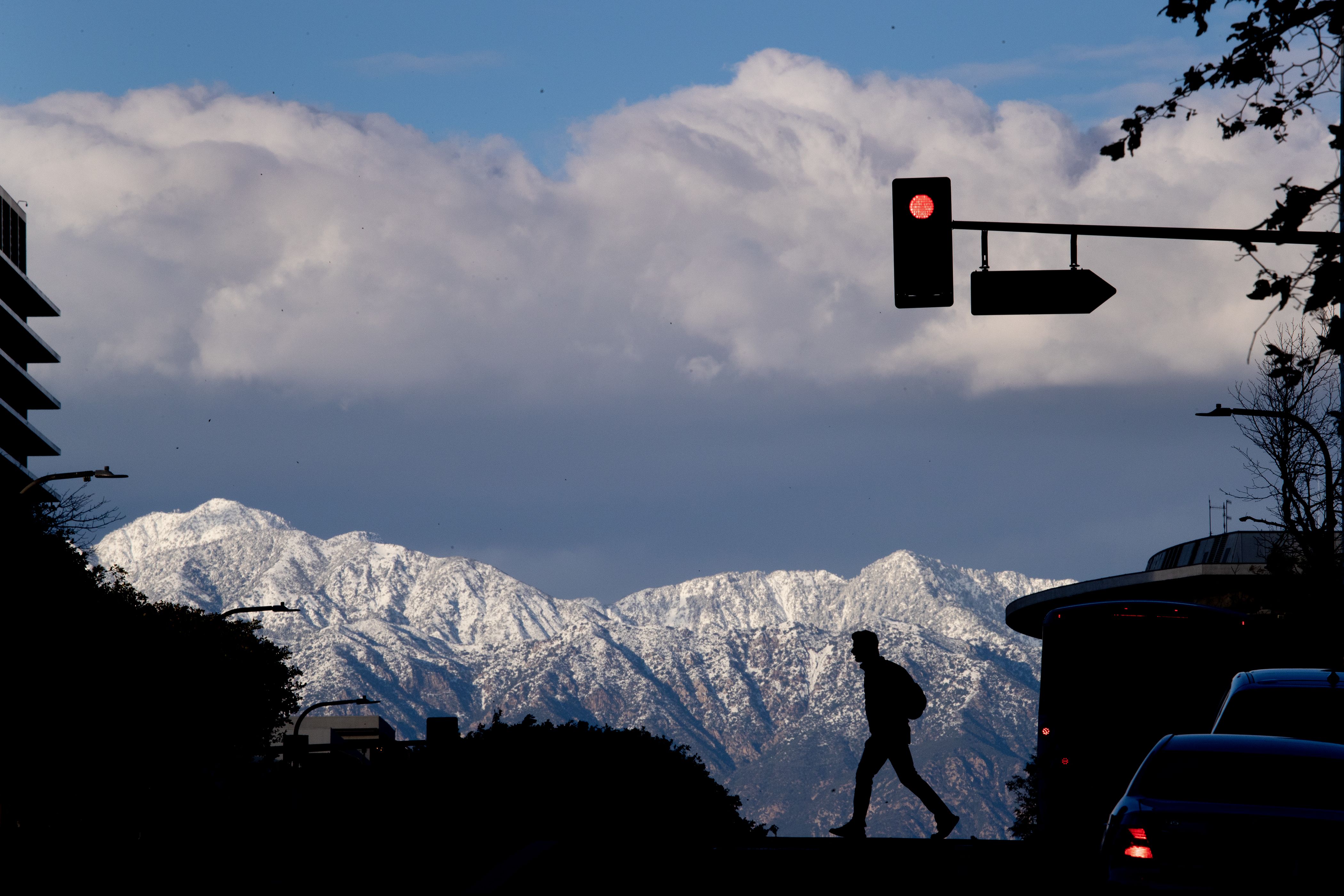 A pedestrian crossing the street in downtown Los Angeles is silhouetted against the snow-capped San Gabriel mountains at sunset after historic rain and snow dumped on Southern California in on Wednesday, March 1, 2023 in Los Angeles.