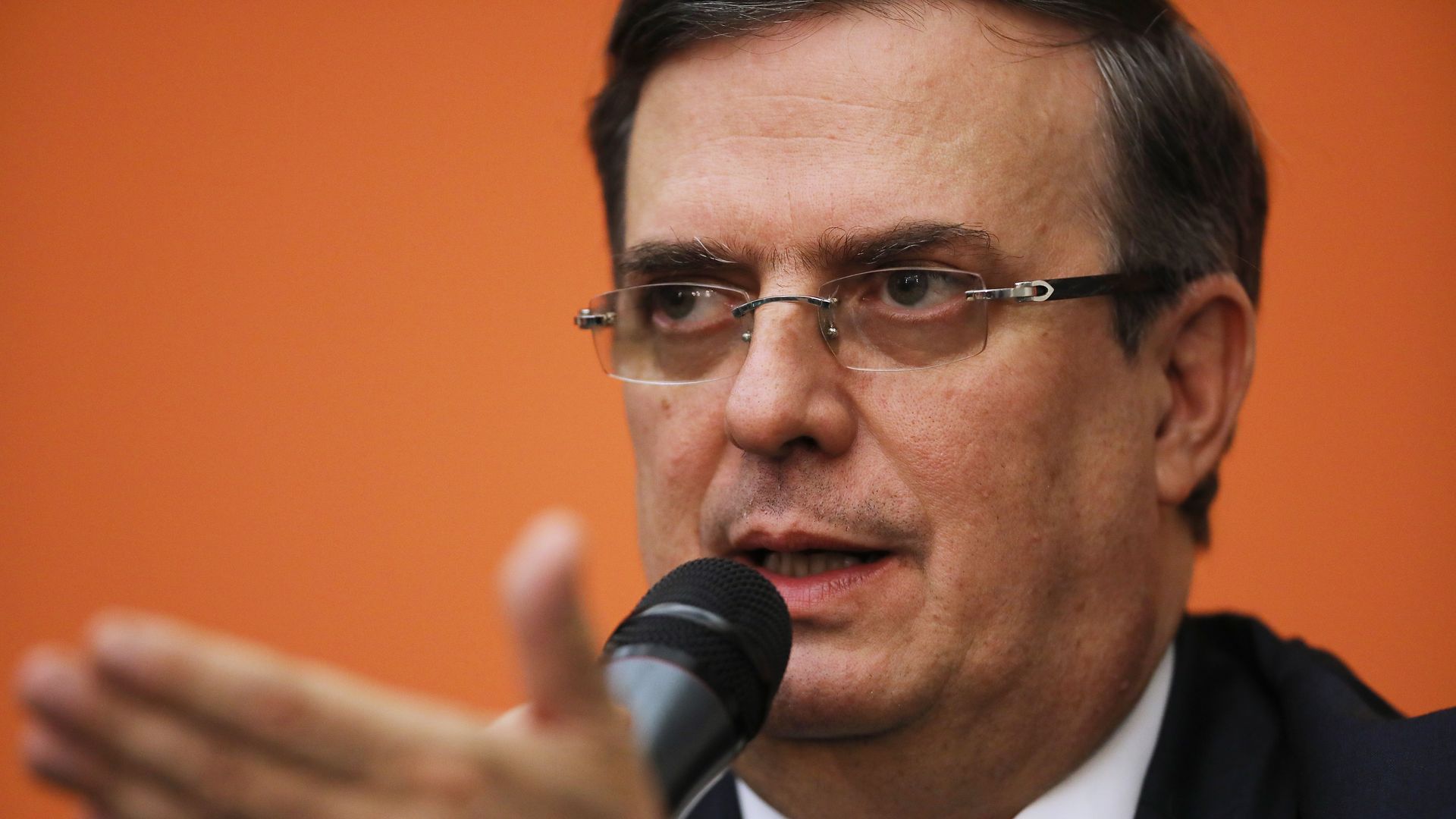 Mexican foreign minister Marcelo Ebrard speaking into a microphone while gesturing his hand in front of his face. 
