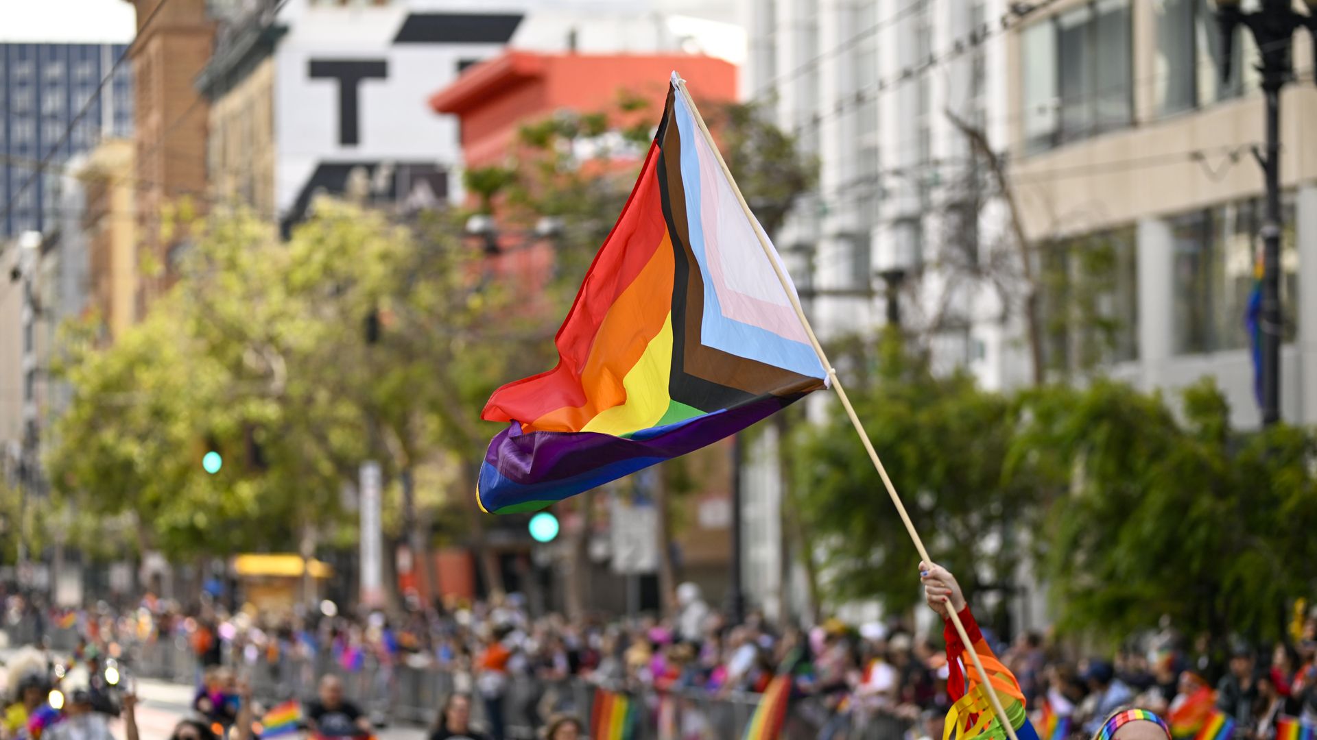 Photo of an LGBTQ pride flag raised in the air as part of a Pride parade in the streets
