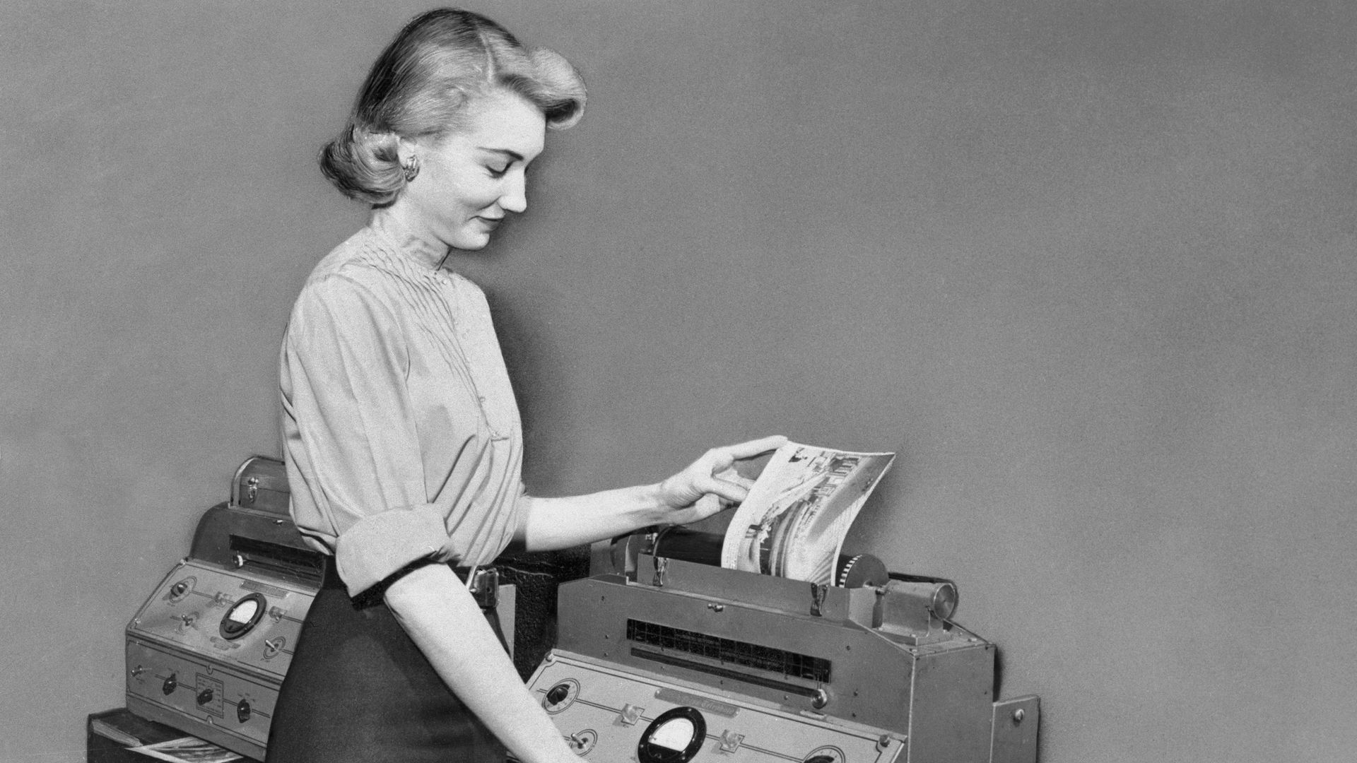 Black-and-white photo of a woman using an antiquated teletype machine