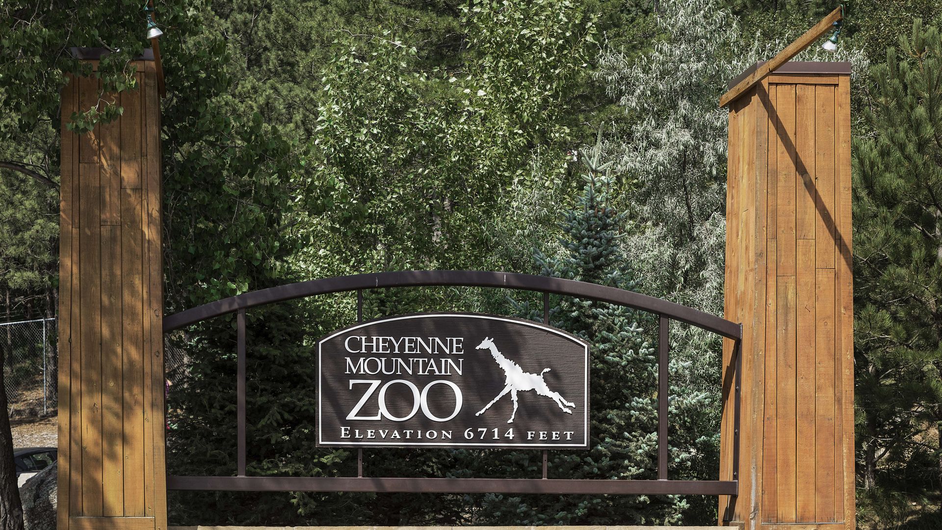 Wooden and stone sign for Cheyenne Mountain Zoo with giraffe silhouette, surrounded by green trees, indicating elevation of 6714 feet.