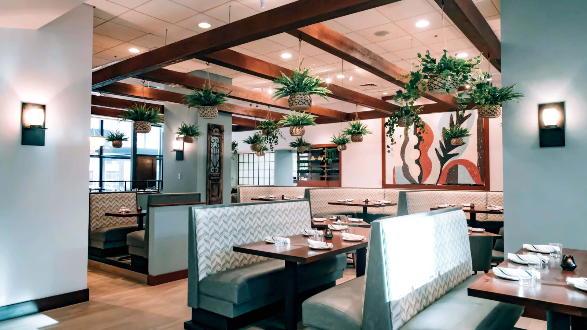 A restaurant with blue booths and wooden tables. Plants hang from the ceiling.