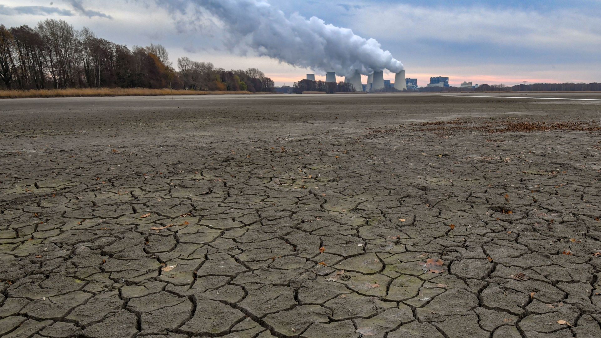 Cracks have formed on the bottom of a drained carp pond, while in the background water vapour rises from the cooling towers of the Jänschwalde lignite-fired power plant of Lausitz Energie Bergbau