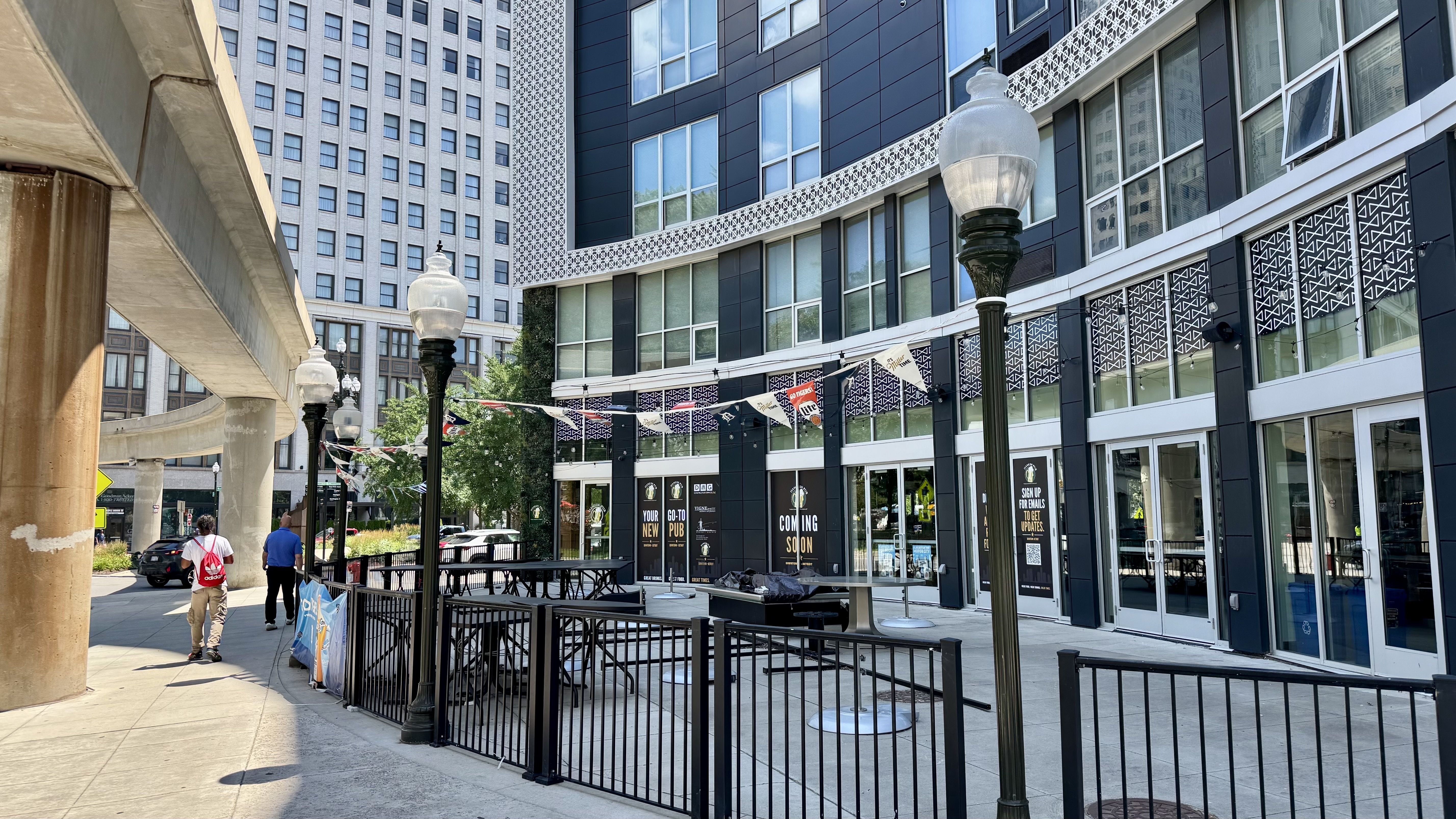 The exterior of a downtown restaurant, with a gate and outdoor seating. The People Mover rail is visible.