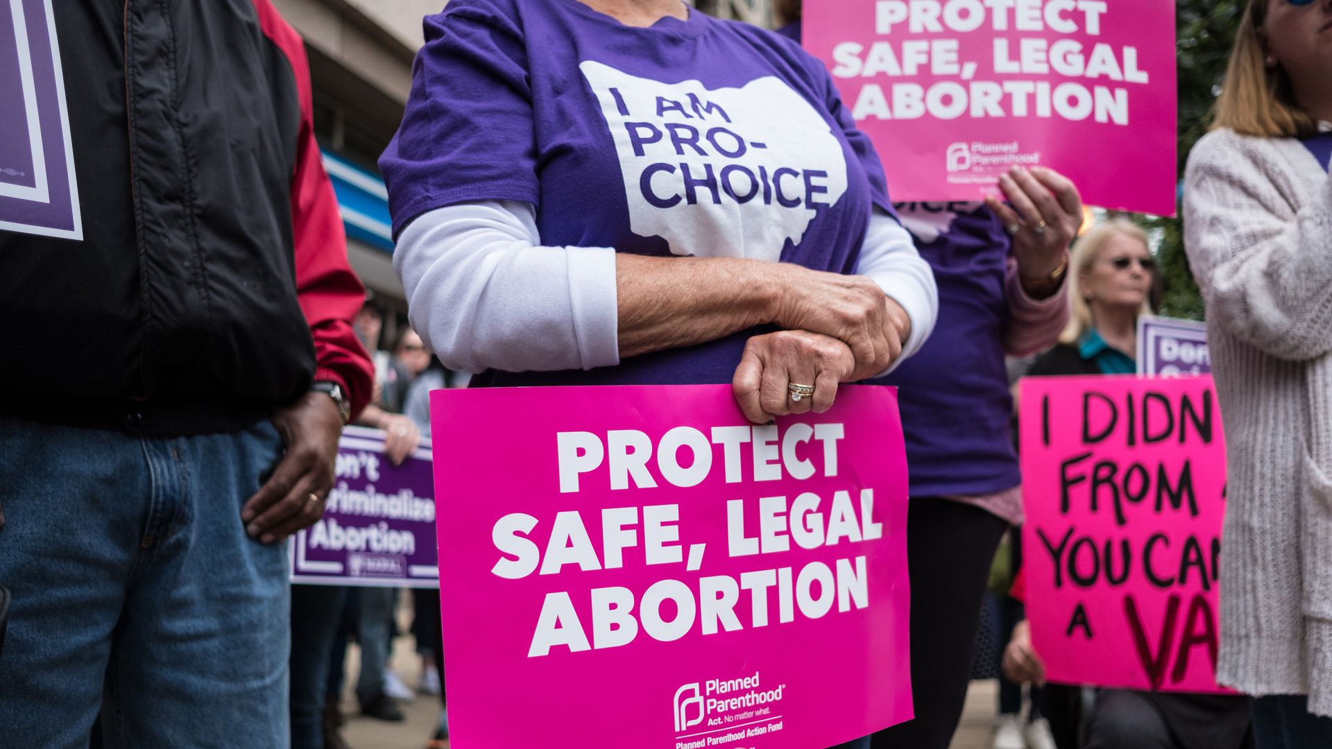 Picture of a person holding a placard that says "protect safe, legal abortion"