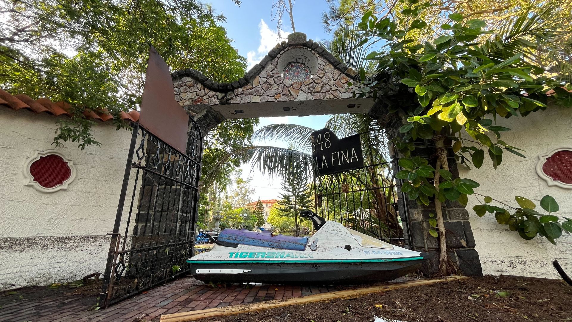 A jet ski thrown by Hurricane Helene's winds lies on a driveway against a broken gate.