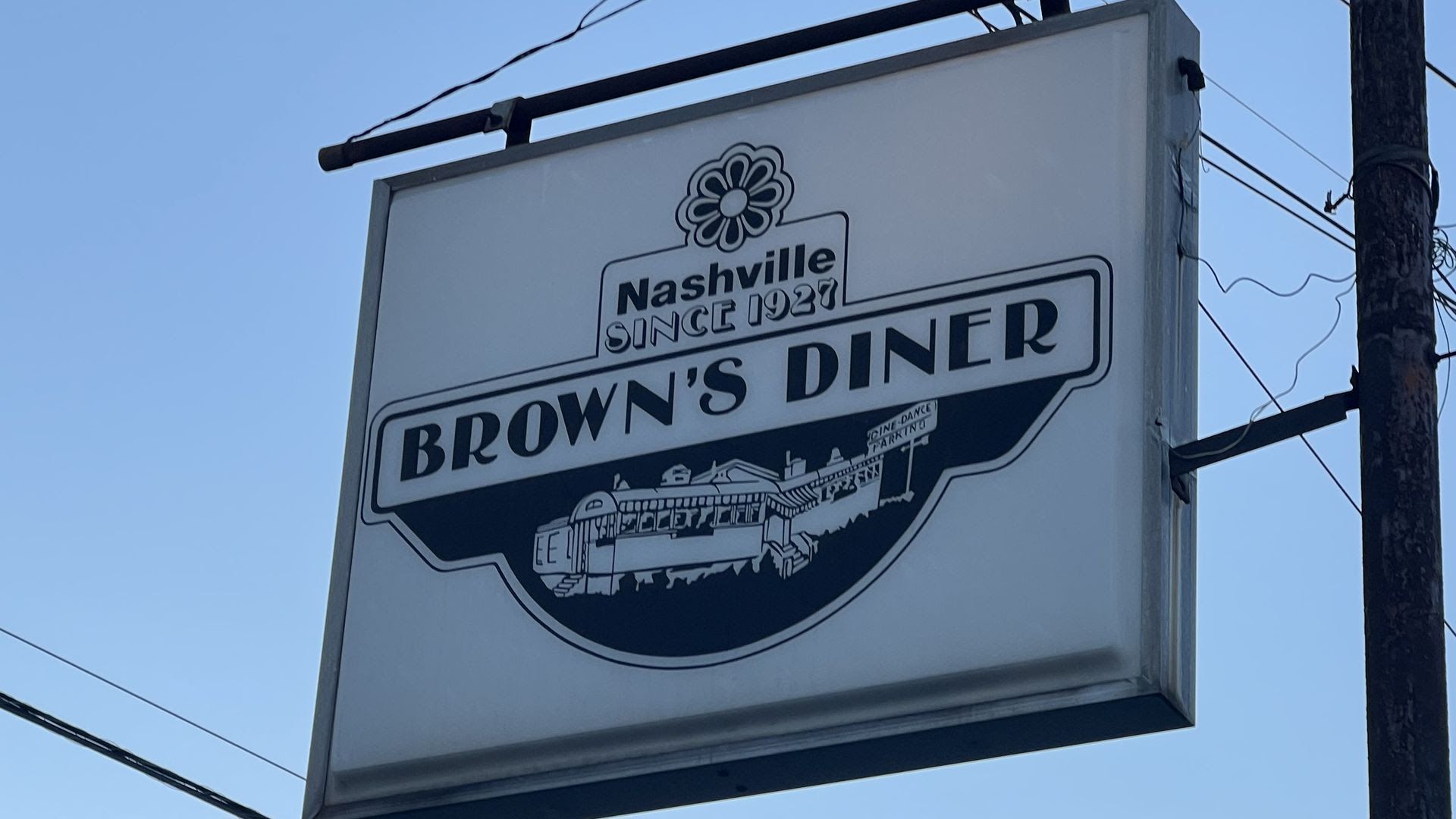 Outdoor sign for Brown's Diner in Nashville, established in 1927, featuring a flower logo and a black-and-white illustration of the diner building against a clear blue sky.