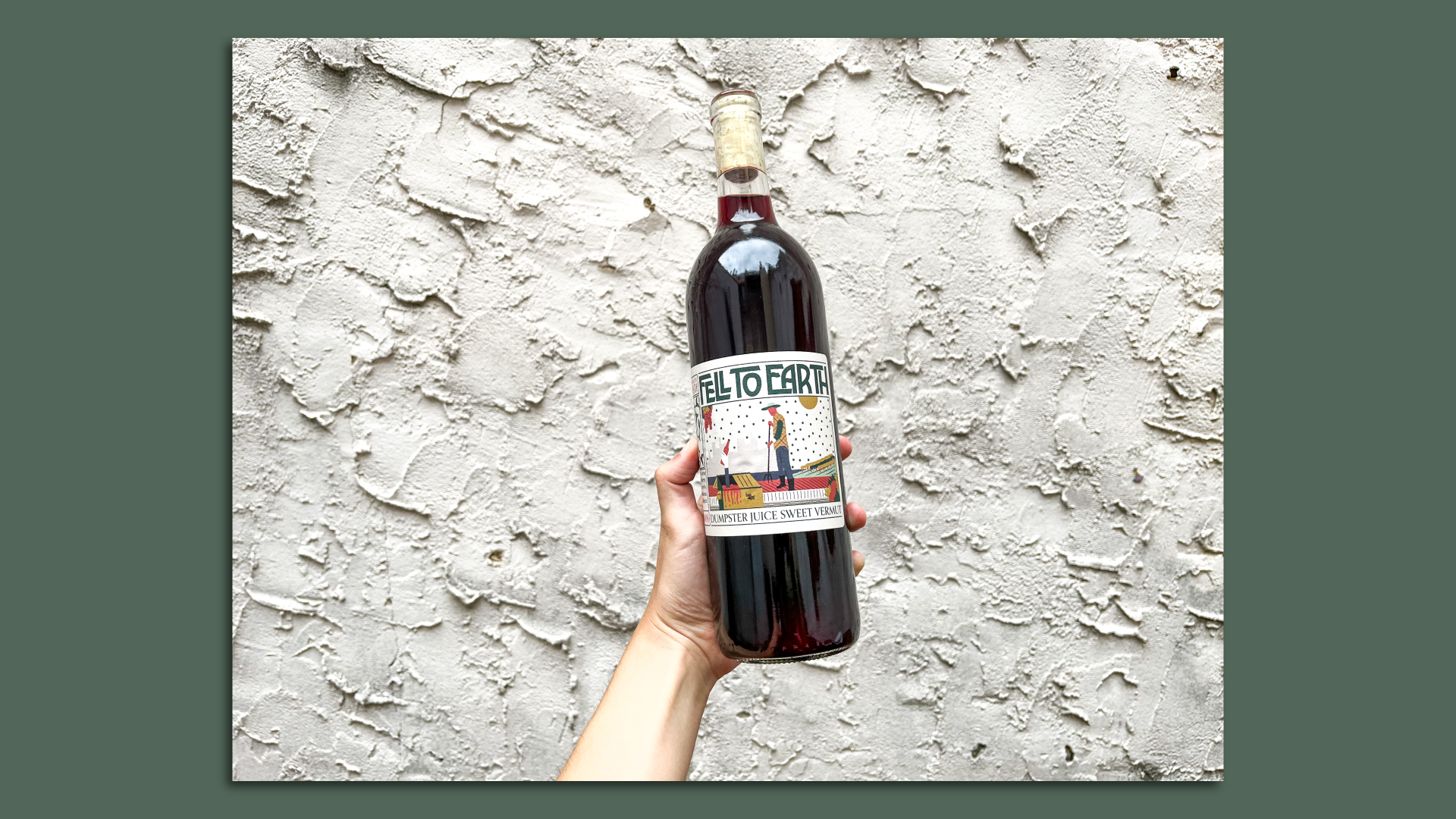 A hand holding up a bottle of the first batch of Dumpster Juice vermouth under the Fell to Earth label.