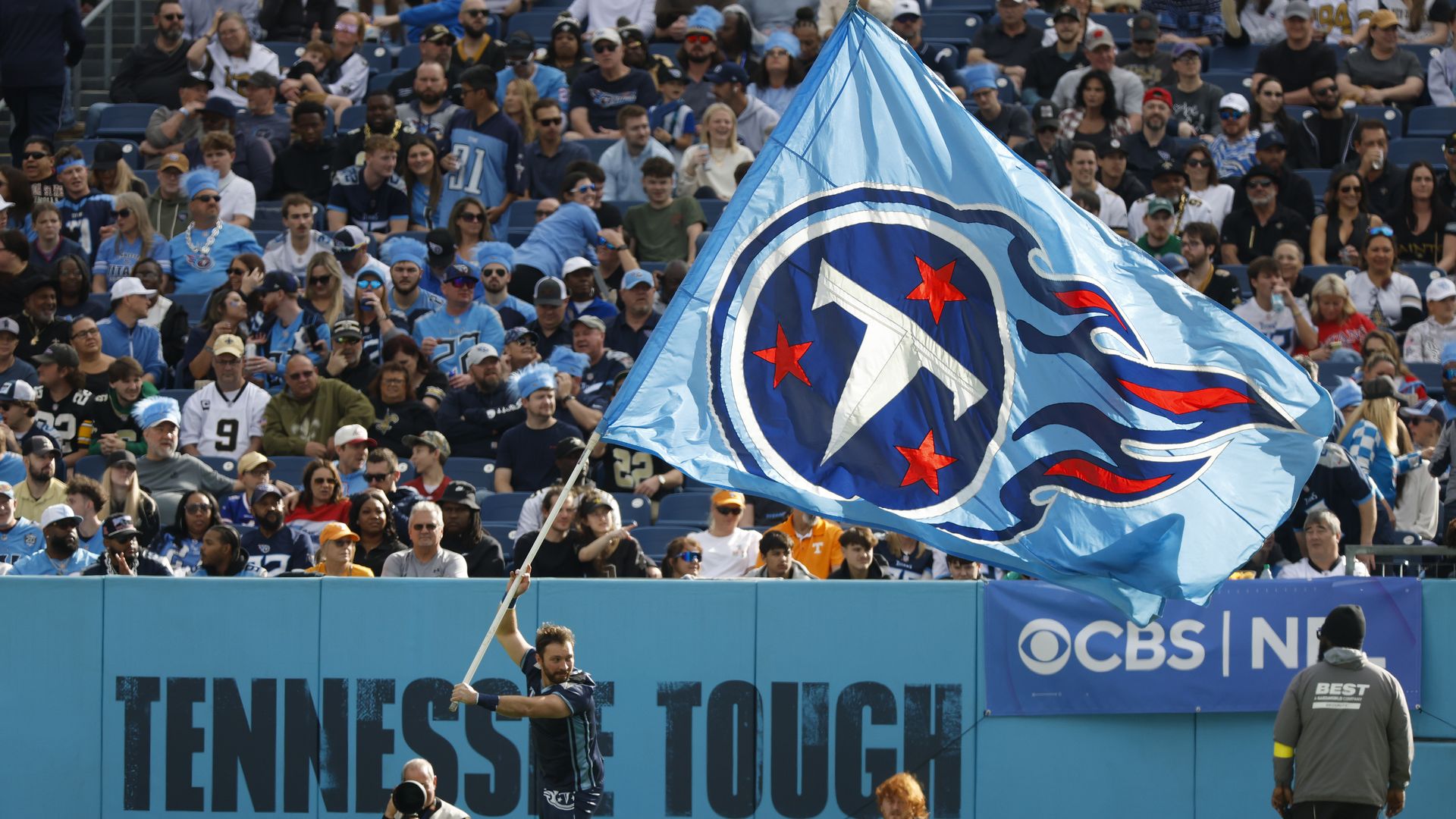 A man waves a Titans flag in front of fans during a game at Nissan Stadium in 2025.