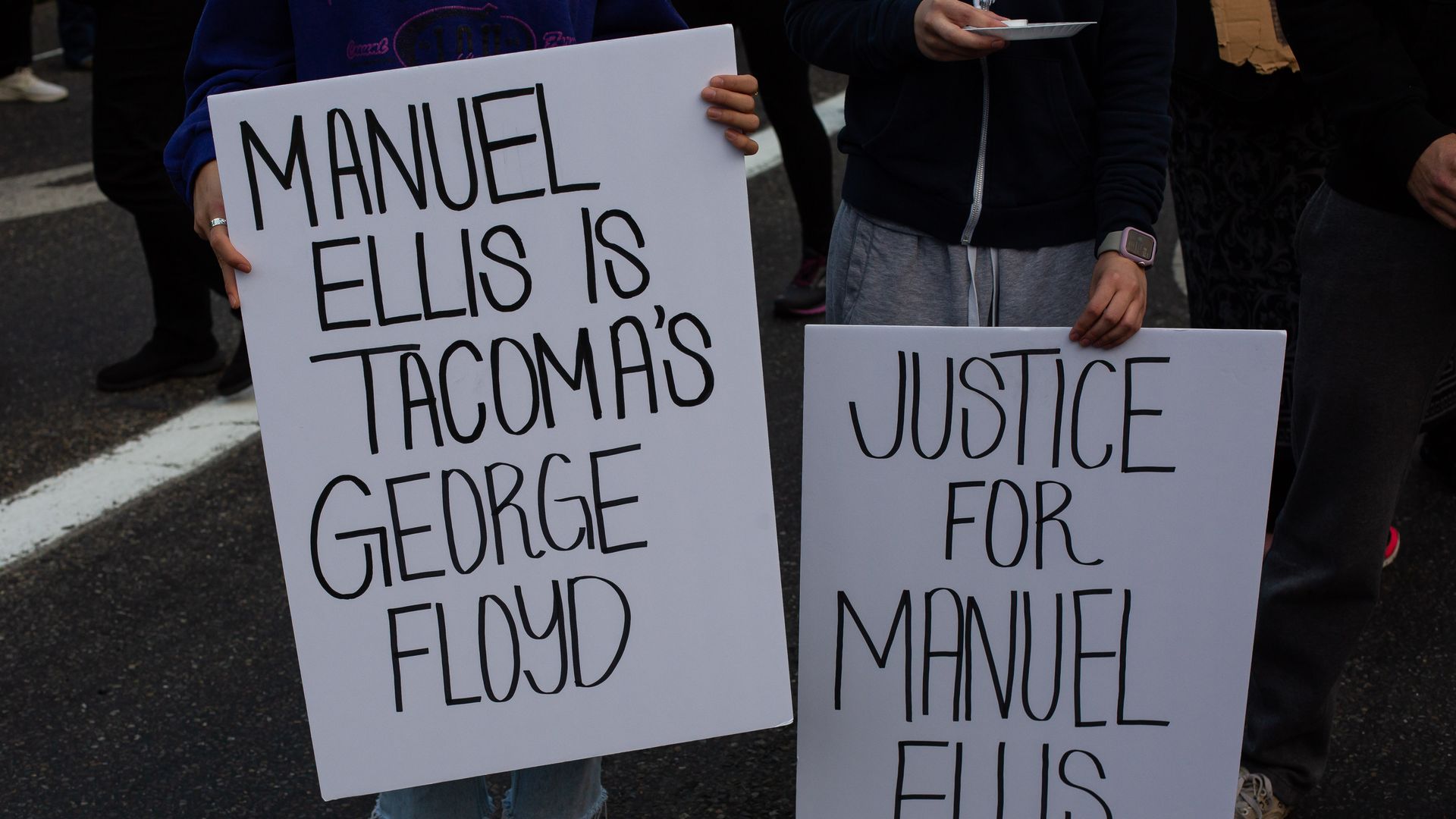 People hold signs during a vigil for Manuel Ellis, a black man whose March death while in Tacoma Police custody