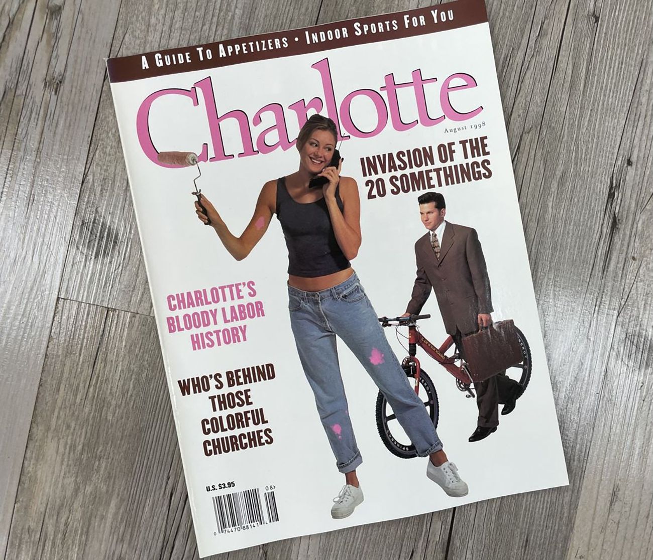 Charlotte magazine cover with a pink logo, a woman in jeans holding a paintbrush, and a man with a briefcase pushing a bike