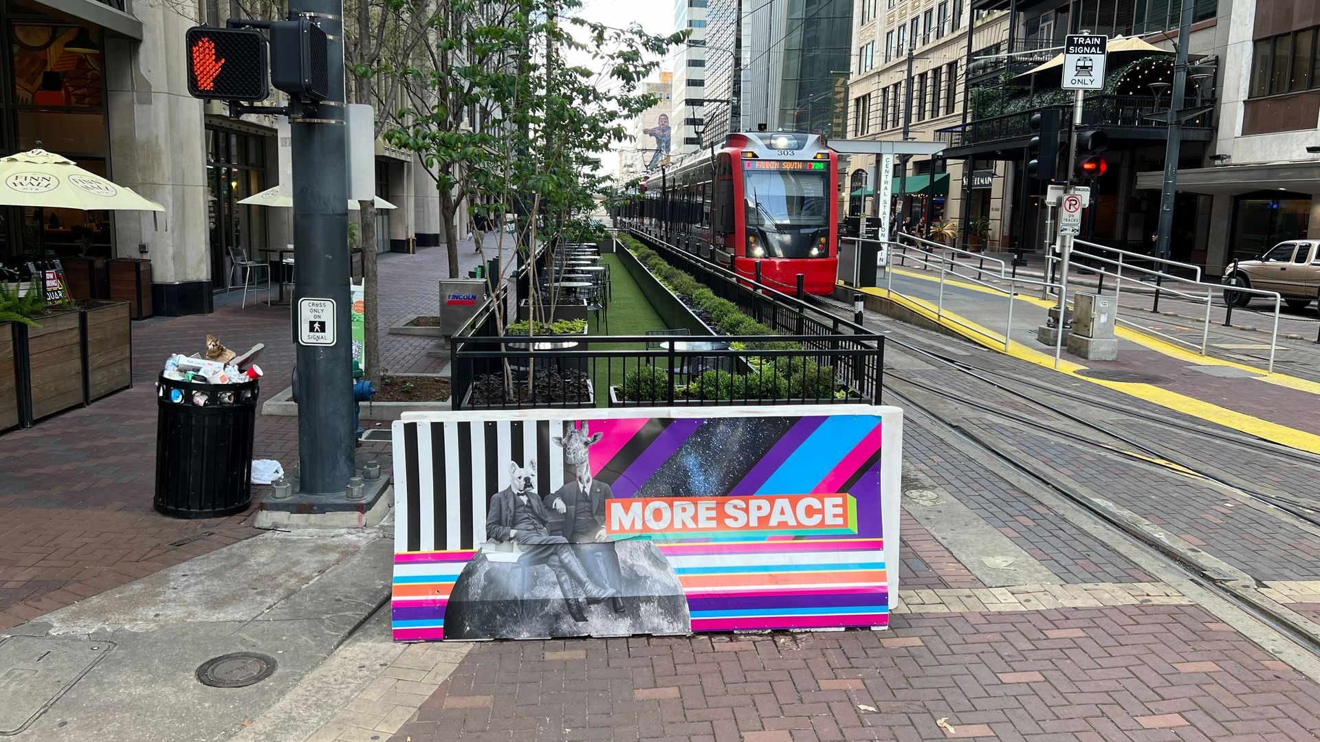 A photo of Main Street in downtown Houston, with a barricade reading "MORE SPACE" and a train in the background