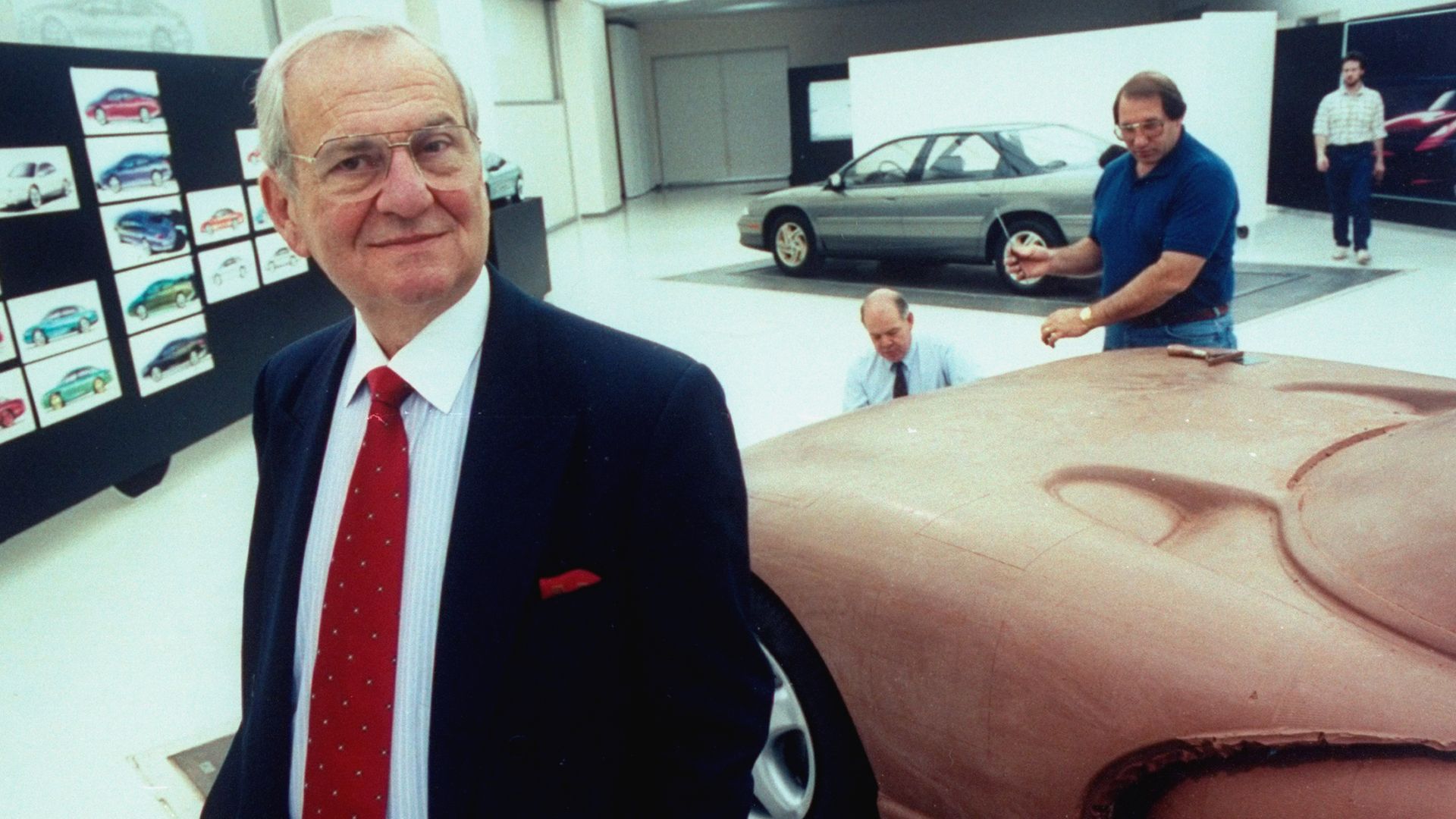 Chrysler Corp. Chmn. Lee Iacocca posing in front of full-sized clay model of the proposed Viper sports car being worked on by staff technicians.