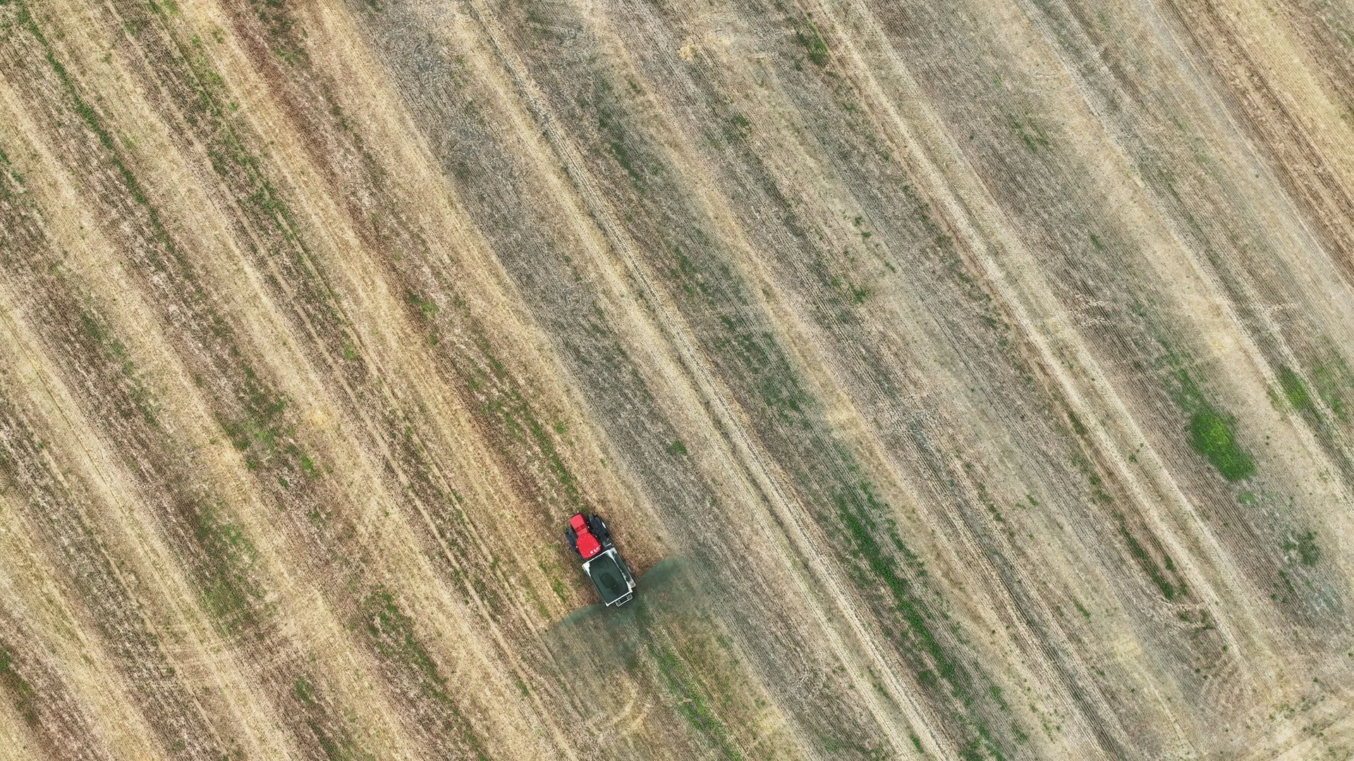 A red tractor, seen from above, spreads basalt rock across a field.
