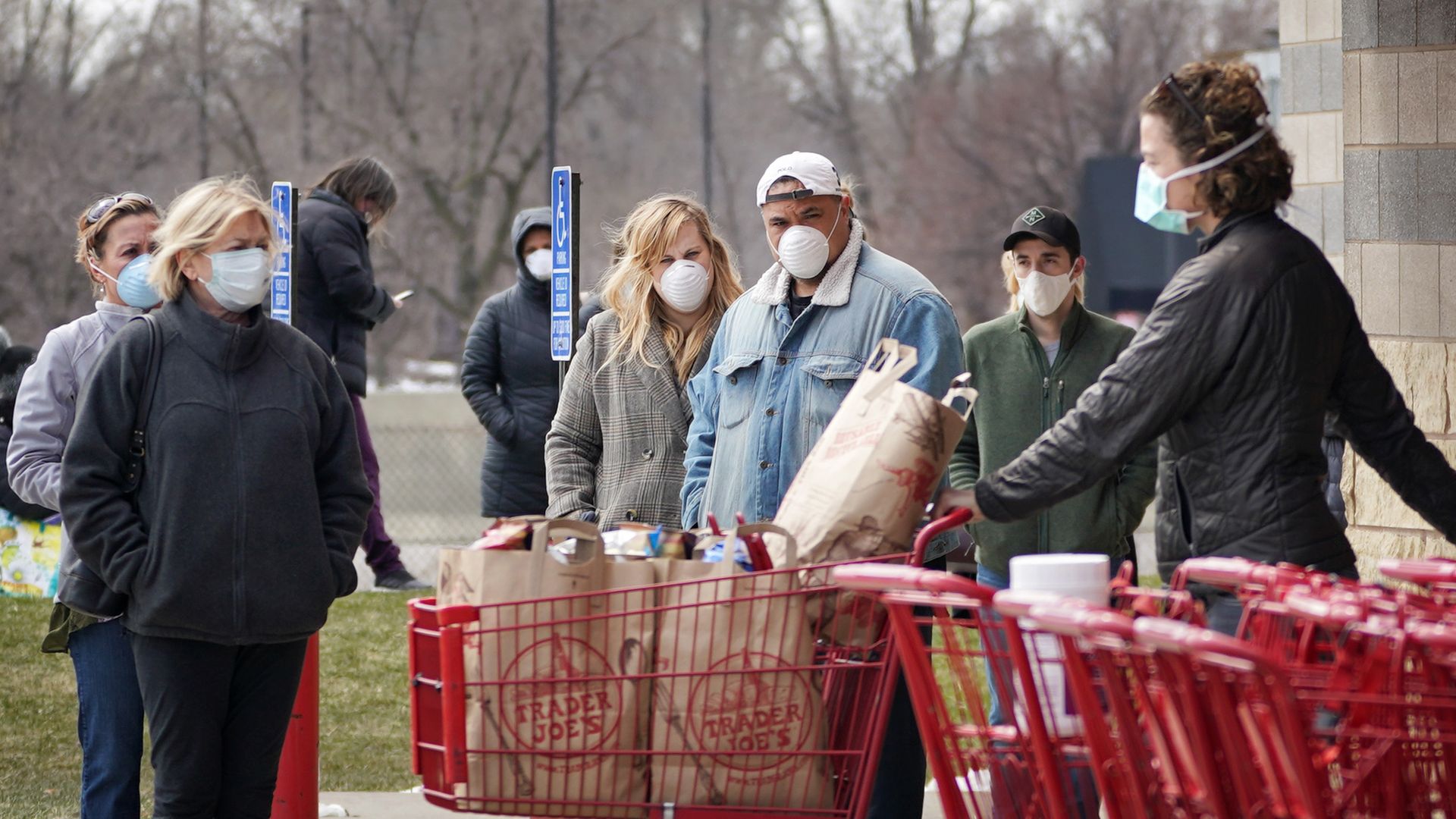 Shoppers stand in facemasks outside a grocery store with shopping cards in the foreground