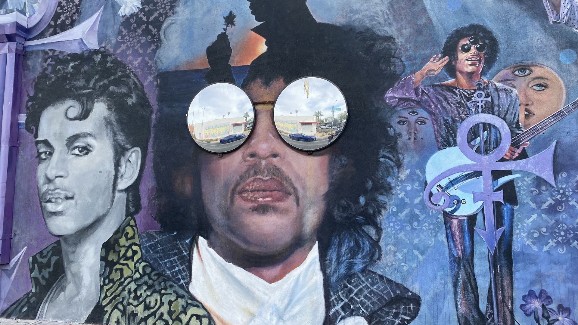 A mural with three images of the musician Prince, with round mirrors forming sunglasses on the face of the middle image.