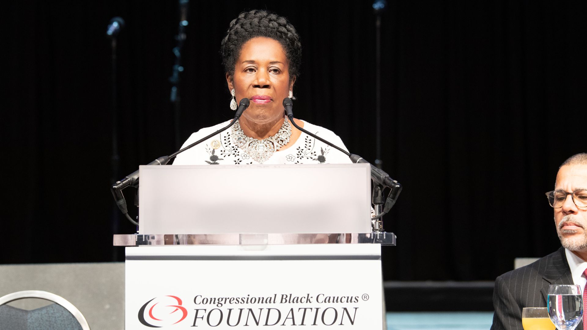 Sheila Jackson Lee at CBC Foundation podium in all white.