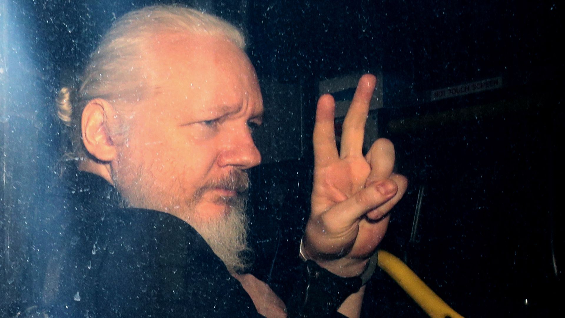 Julian Assange with his hand in a peace sign.
