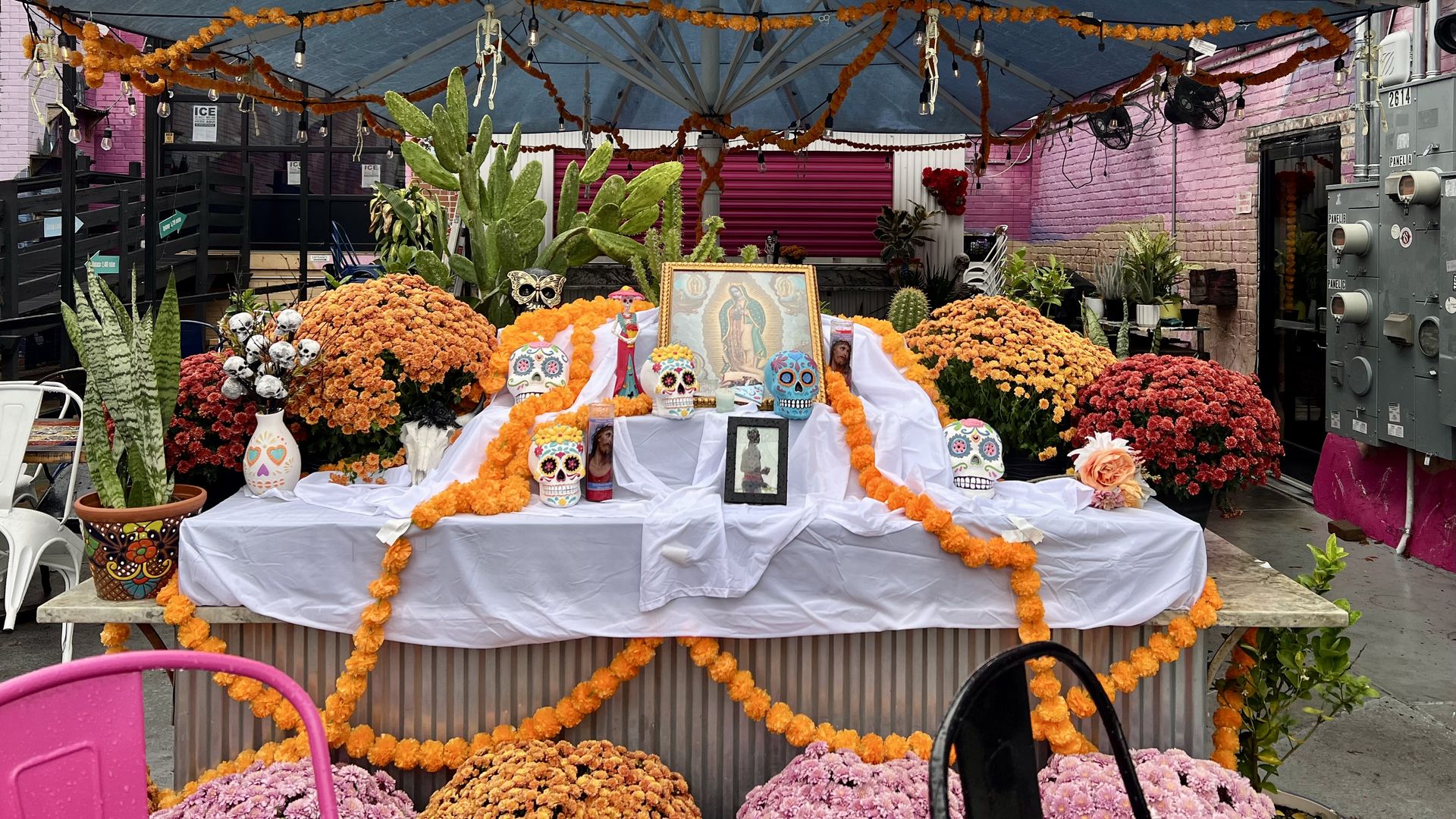 Colorful Day of the Dead altar with marigold garlands, painted sugar skulls, religious candles, and an image of Our Lady of Guadalupe, surrounded by vibrant flowers and greenery.