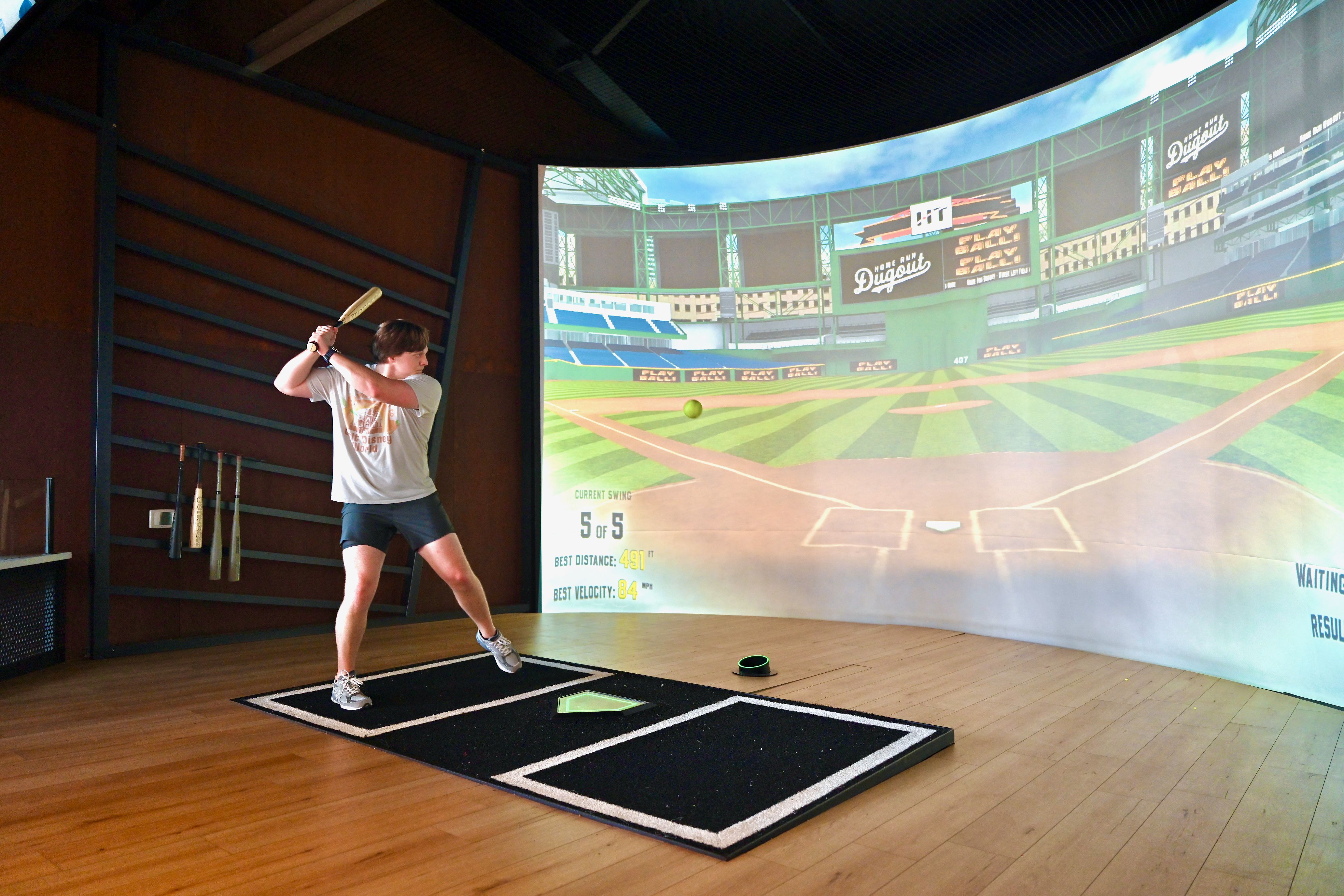 A batter in front of a screen showing a baseball field.