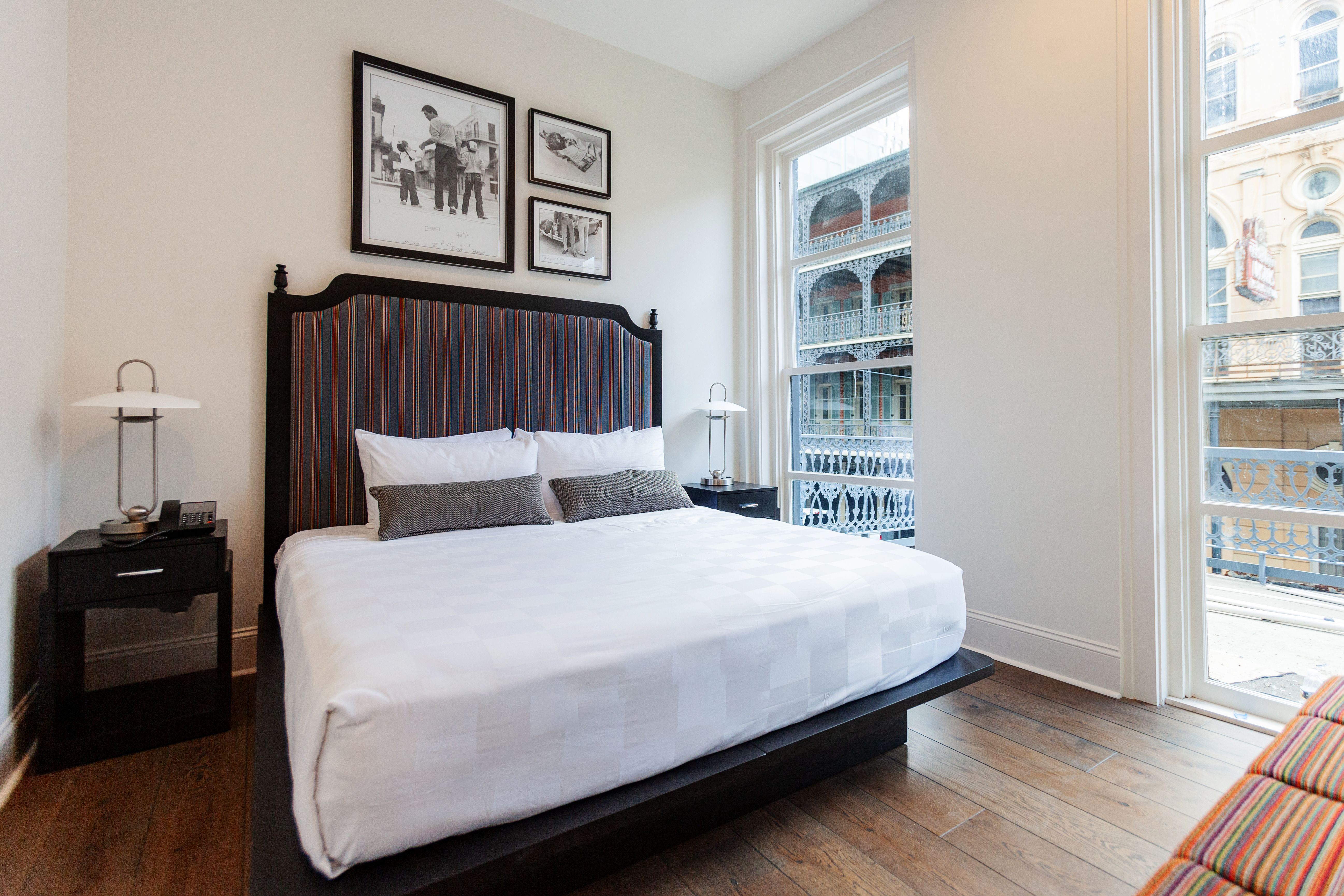 A freshly-made made is seen in a hotel room. Floor to ceiling windows separate the bedroom from a balcony.
