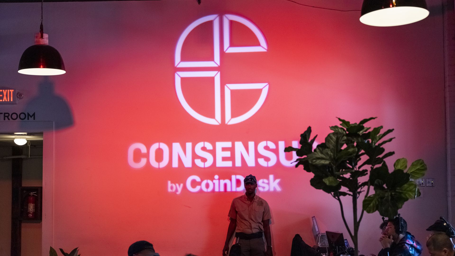 A person standing in front of a red wall with the logo for Consensus.