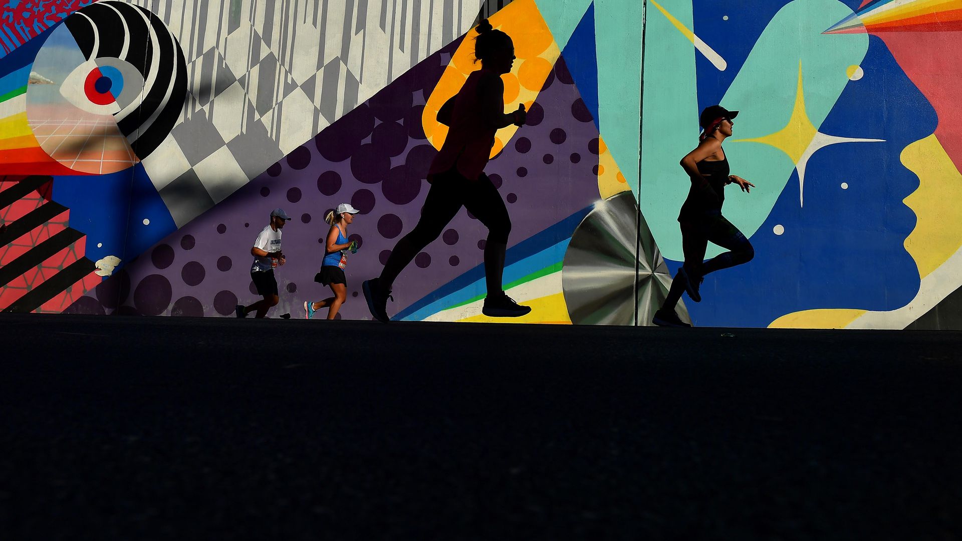 A group of people runs past a colorful mural. 