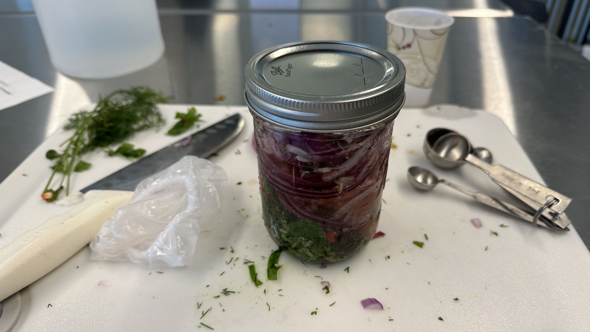 A jar with vinegar, herbs and onions on a cutting board.