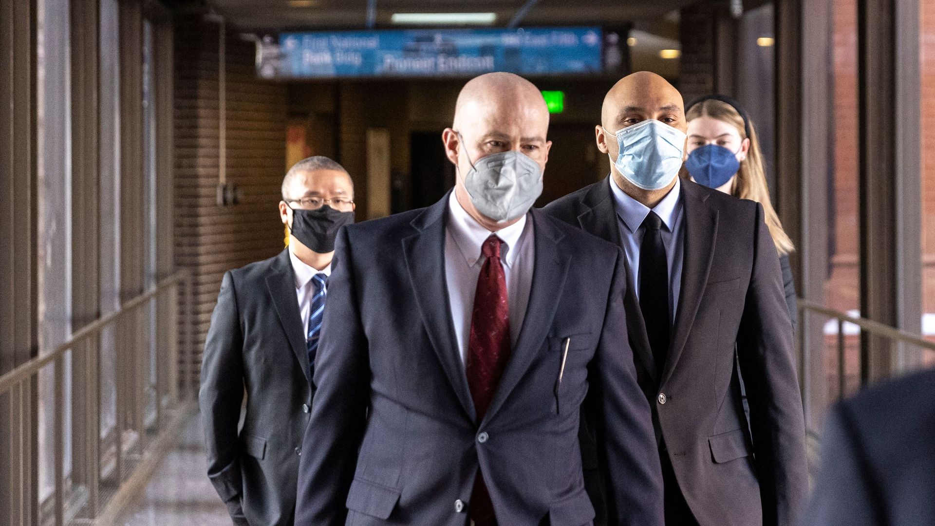 Photo of three masked men and a masked woman in the back walking down a hallway