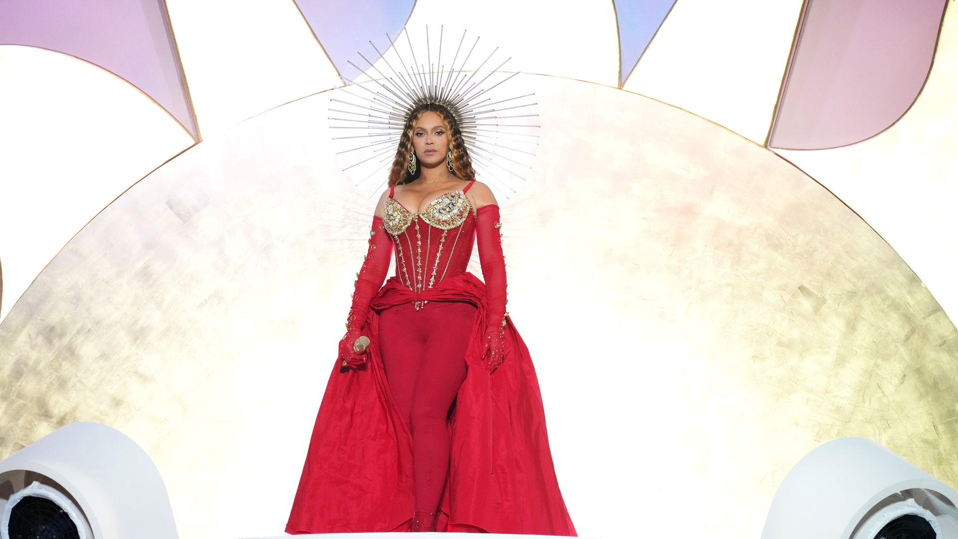 Beyoncé, wearing a red dress and large crown, stares straight ahead while performing 