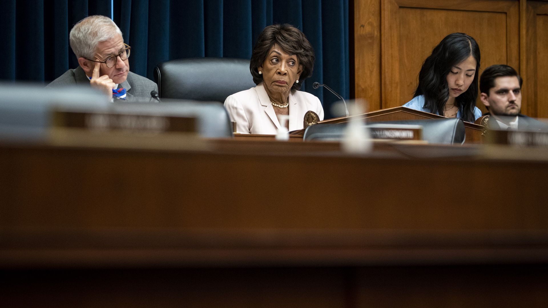 Reps. Patrick McHenry, wearing a grey suit and blue bowtie, and Maxine Waters, wearing a white pantsuit and pearl necklace, sit behind the dais at a Financial Services Committee hearing.  