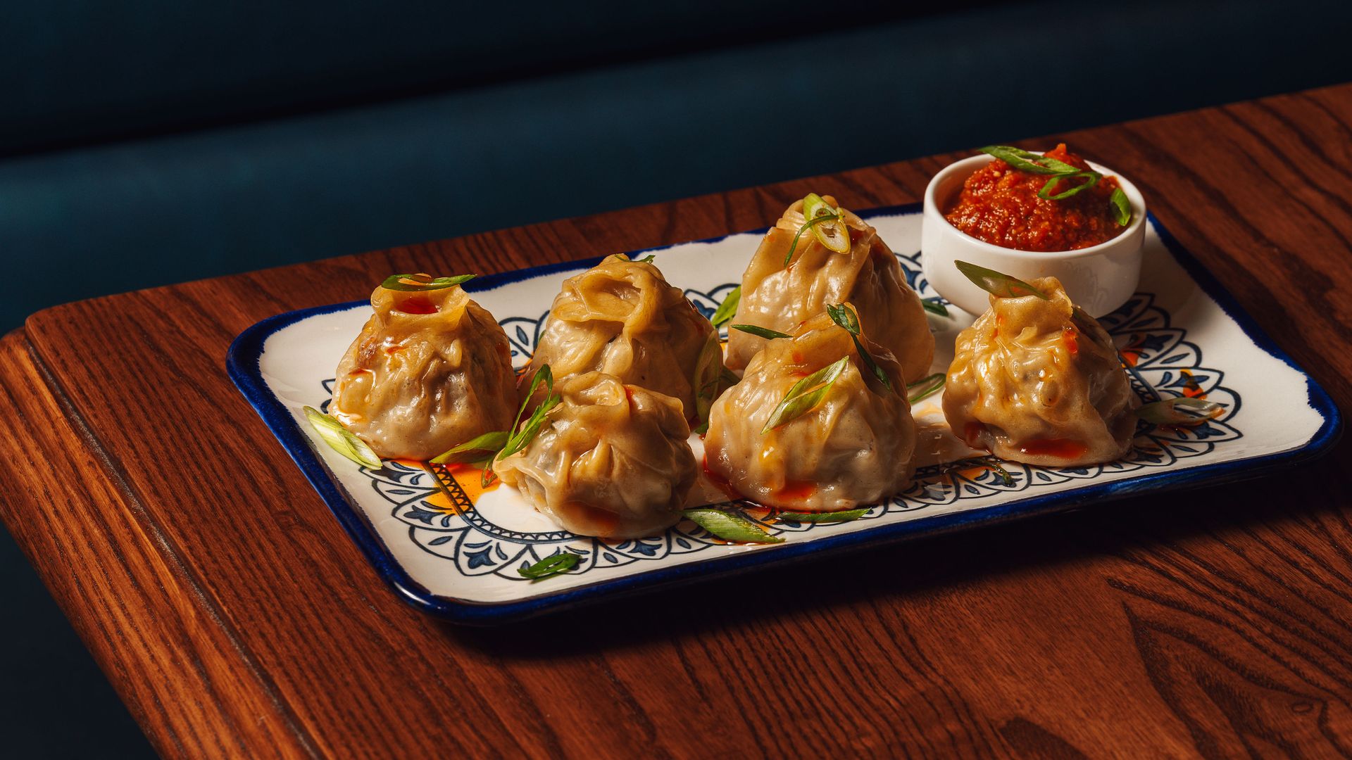 Momo dumplings on a white platter sit on a wooden table