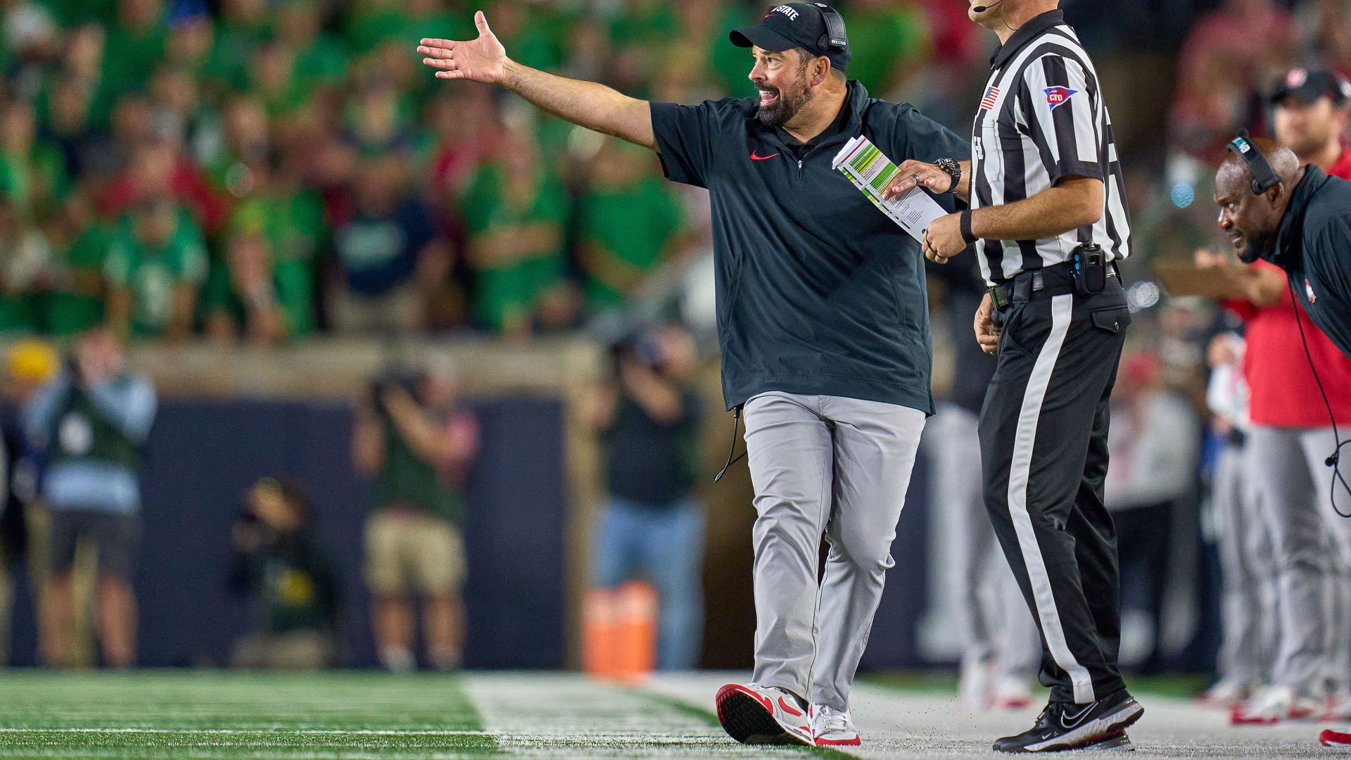 Ohio State football coach Ryan Day walking the sidelines next to a referee.