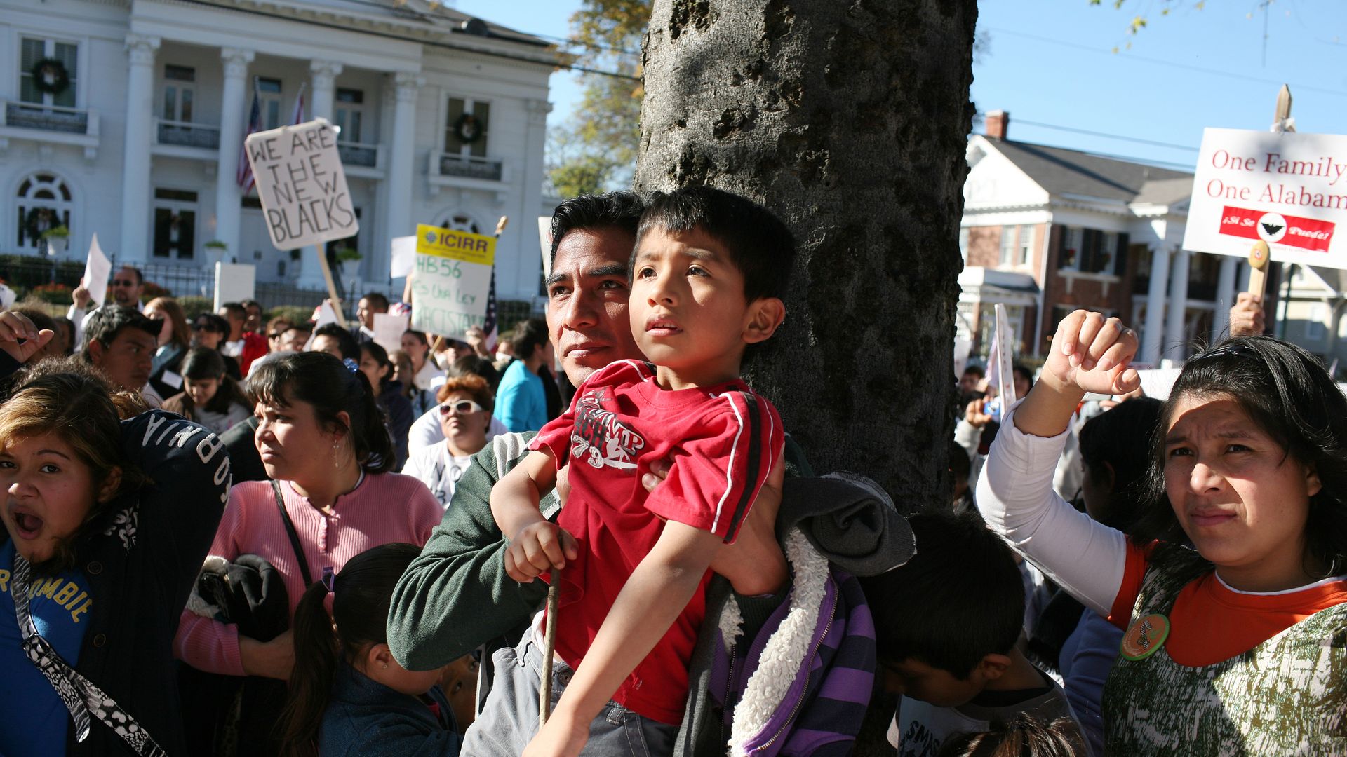 A Latino man lifts up his son to see a speaker at a rally in Alabama in front of the Governor's home in Montgomery, Alabama.