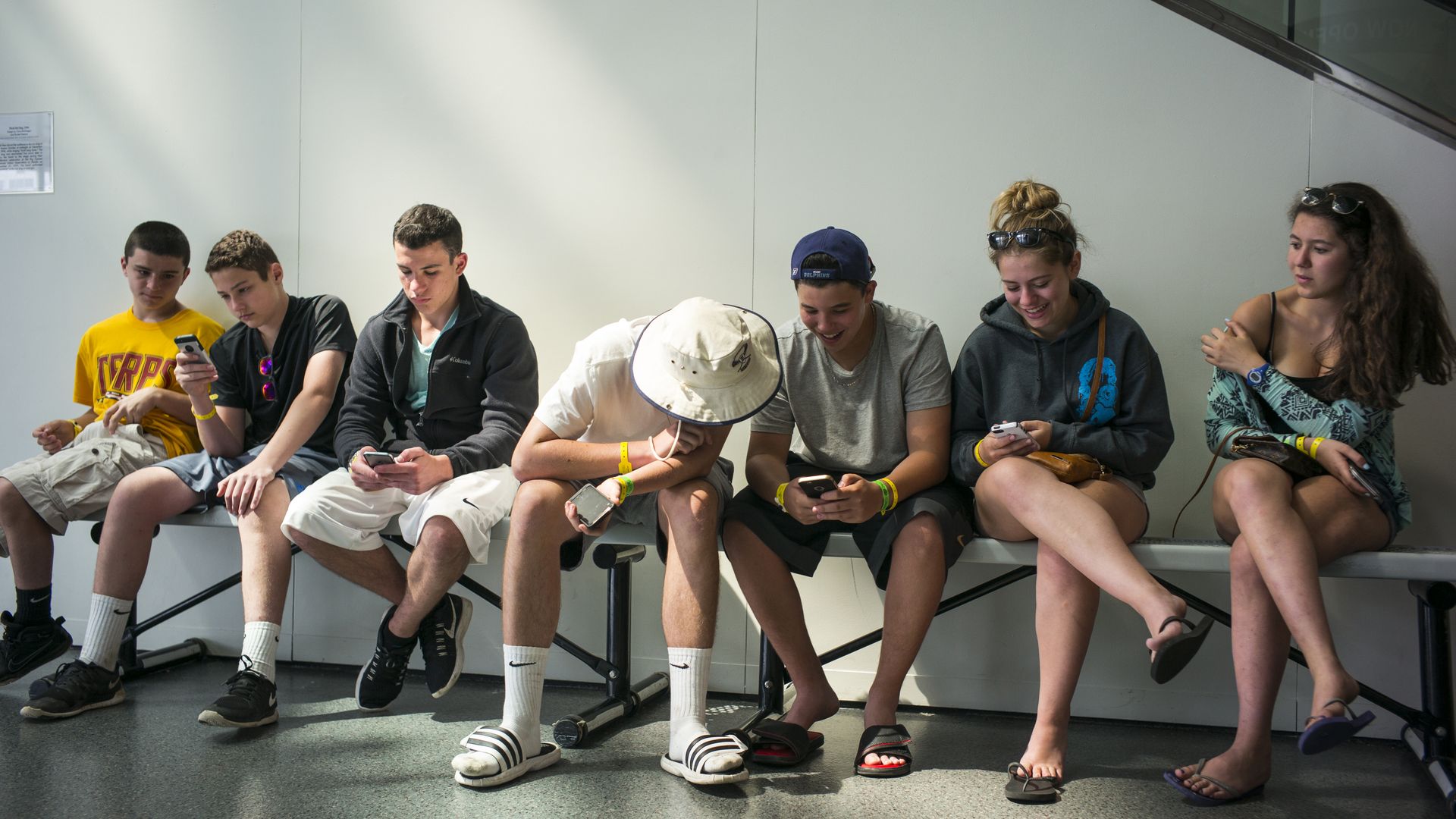 Teenagers sitting on a bench and looking at their smartphones.