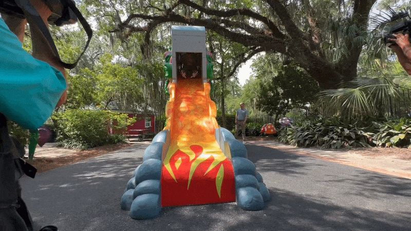 A man slides down a fire-themed slide with his hands in the air.