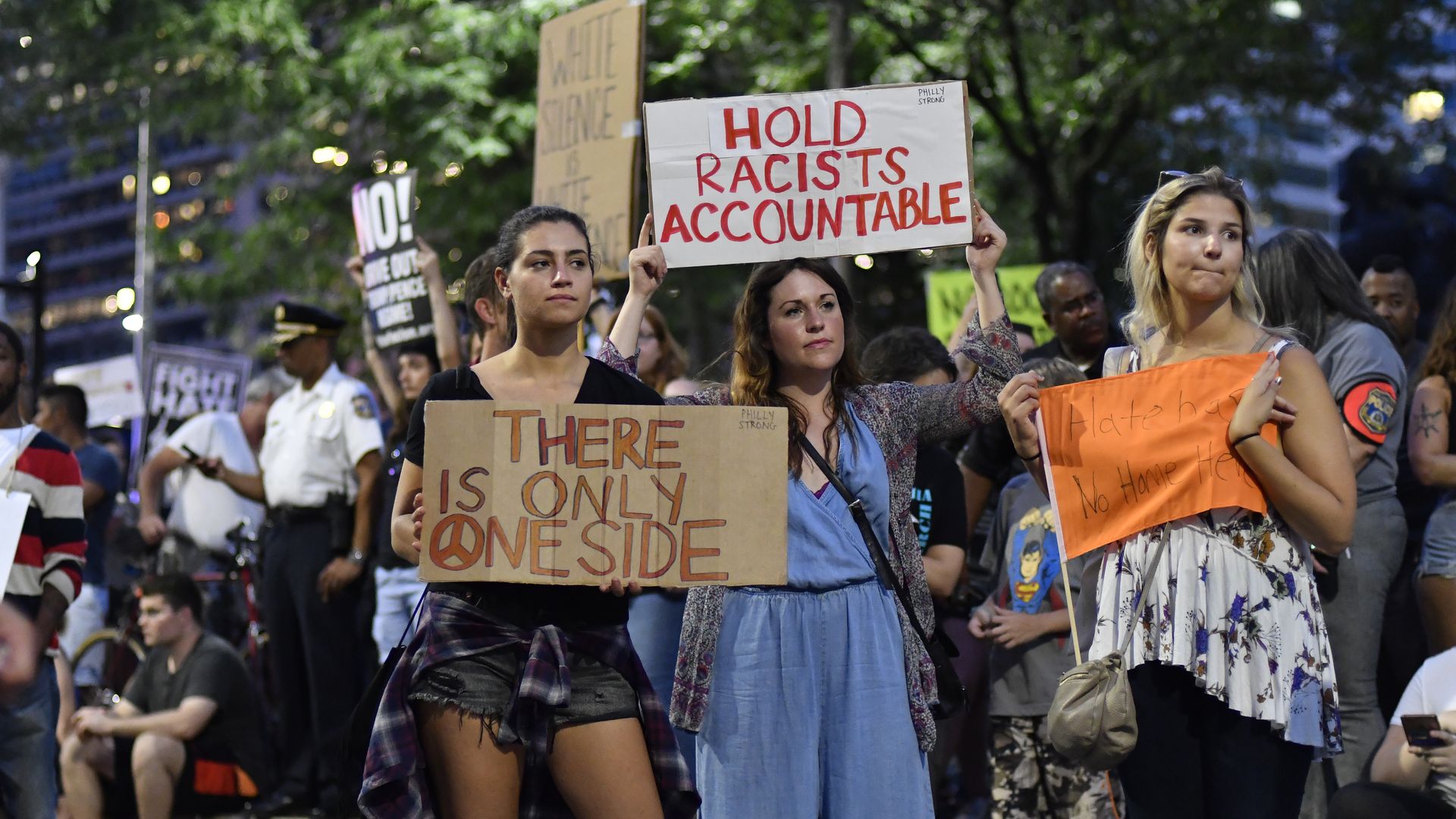 Young women hold signs that read "Hold racists accountable," and "There is only one side." 