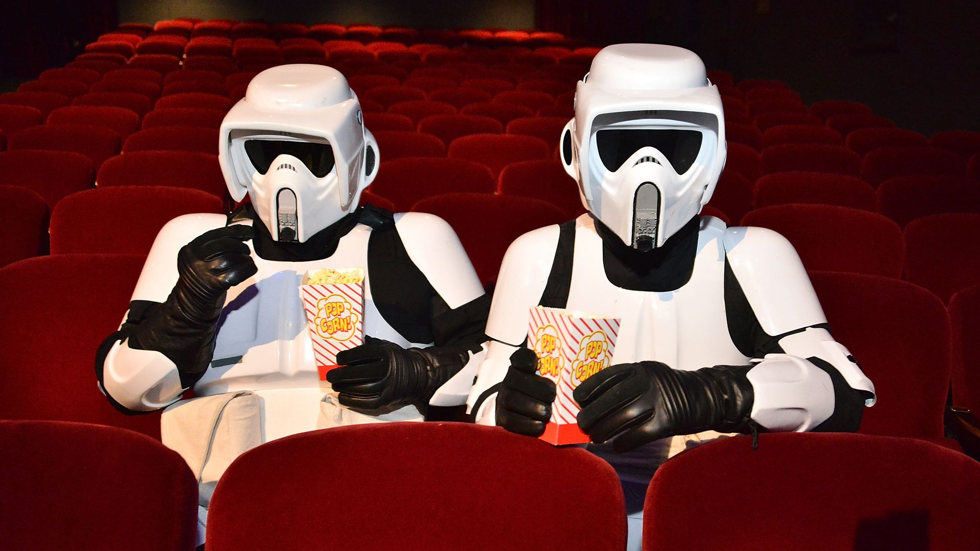 Two fans dressed as stormtroopers eat popcorn in movie theater seats