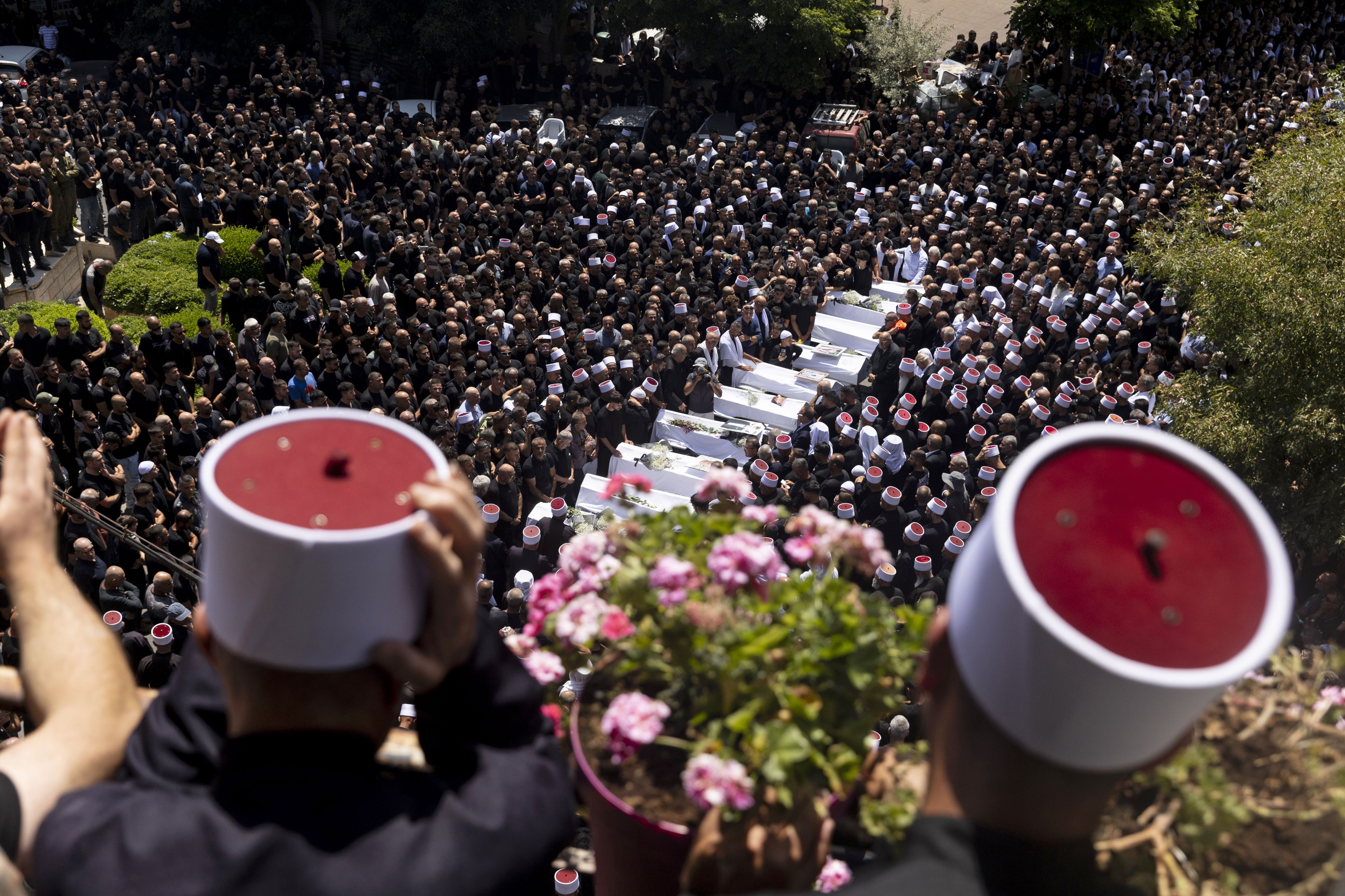 A bird's eye view of large crowds around white caskets