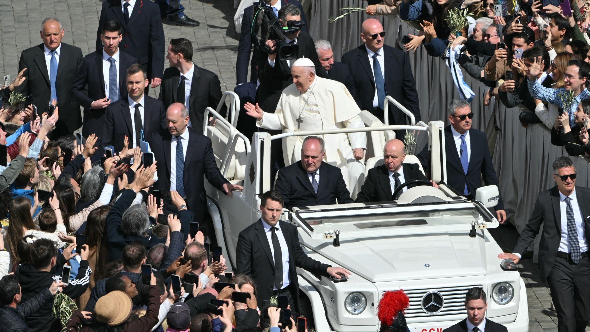 Pope Francis greets the crowd from the popemobile surrounded by bodyguards at the end of the Palm Sunday mass at St Peter's square in the Vatican on March 24, 2024. 