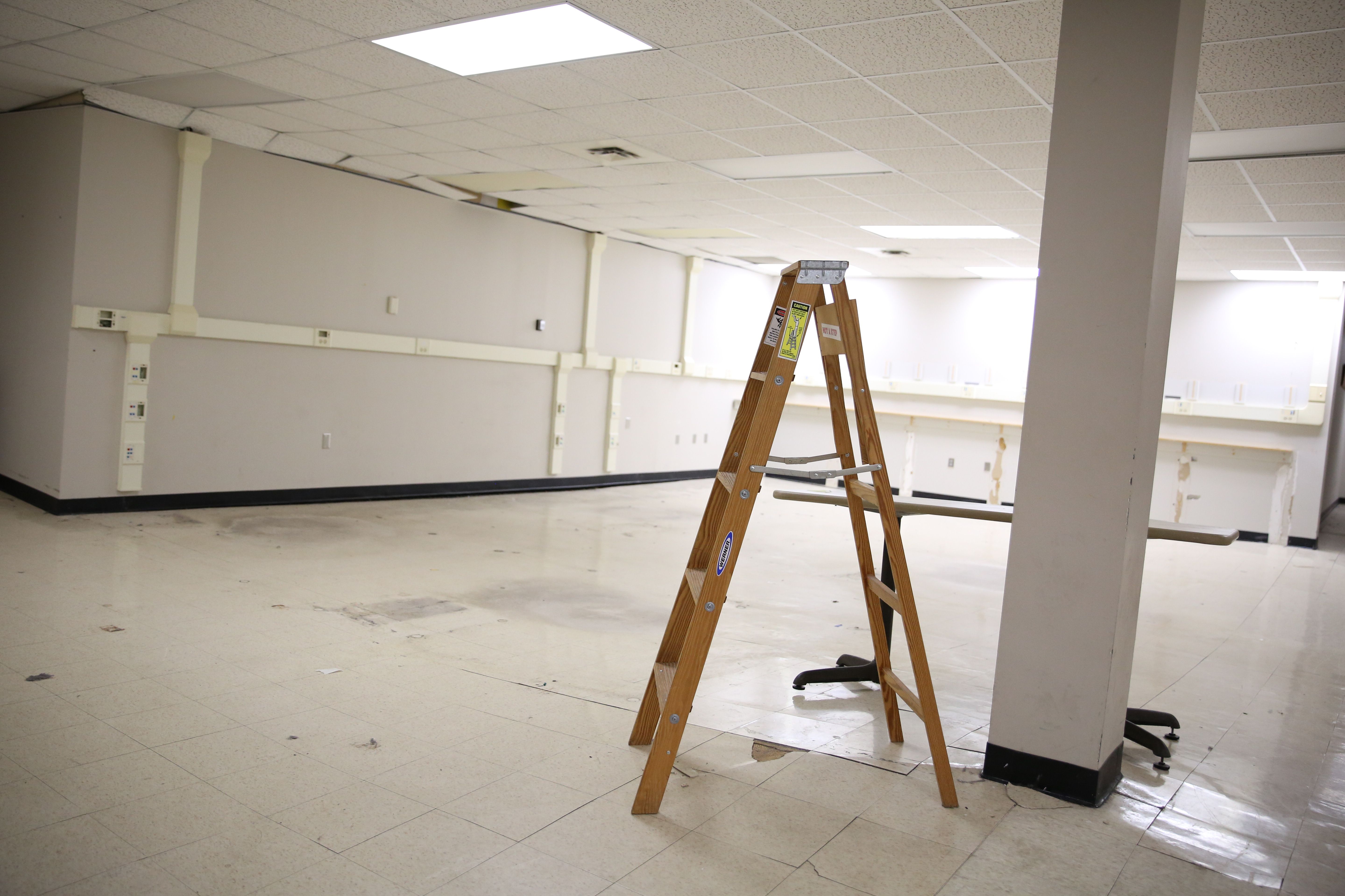 A cleared out room at the former tech center in the 4825 Troost building shows warped and buckling floors that are separating from the walls and ceiling tiles that are getting displaced by the moving walls. A latter stands in the foreground on cracked floor tiles.