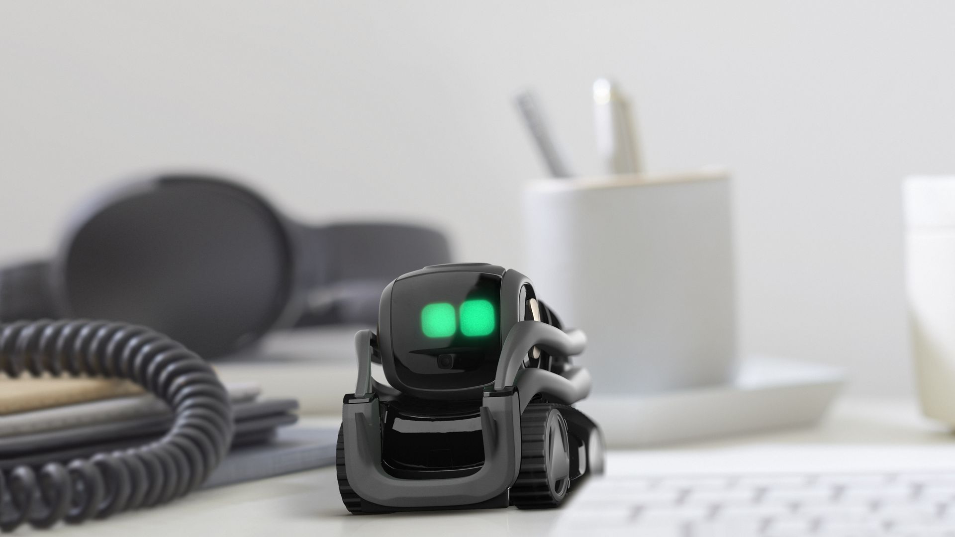 A small mobile robot with green eyes on a desk