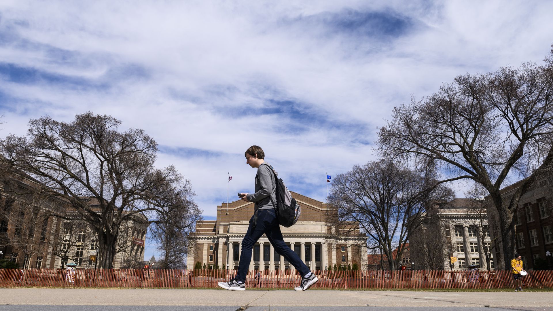 student walks in front of U of M building with bare trees