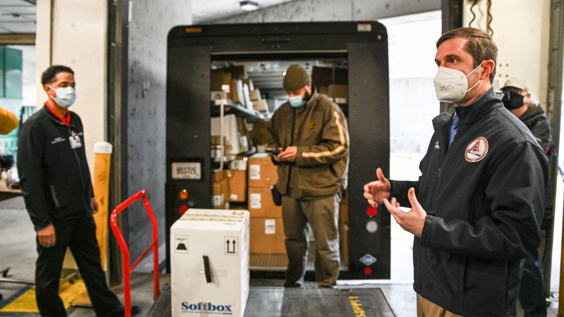 Photo of a masked Andy Beshear speaking to press at a loading dock