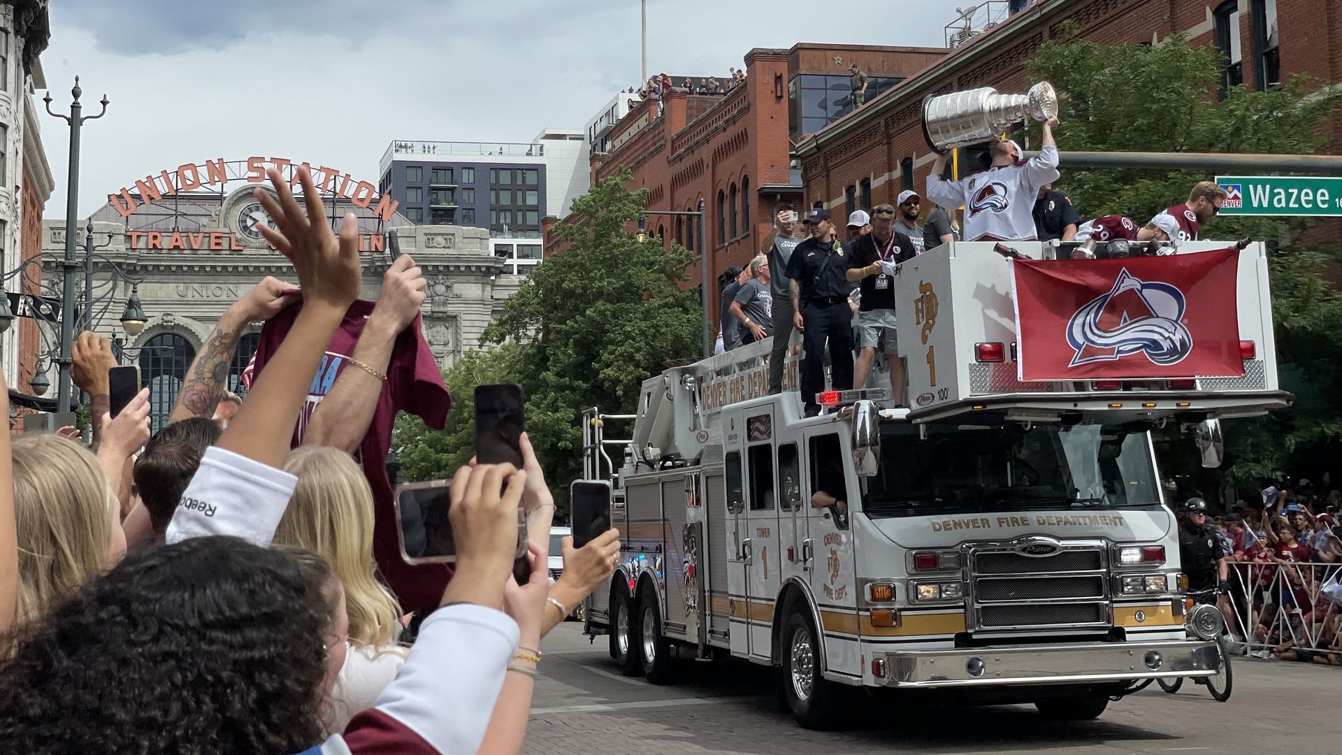 A Colorado Avalanche player celebrates by lifting the Stanley Cup while standing on top of a Denver Fire truck during the Avs victory parade.