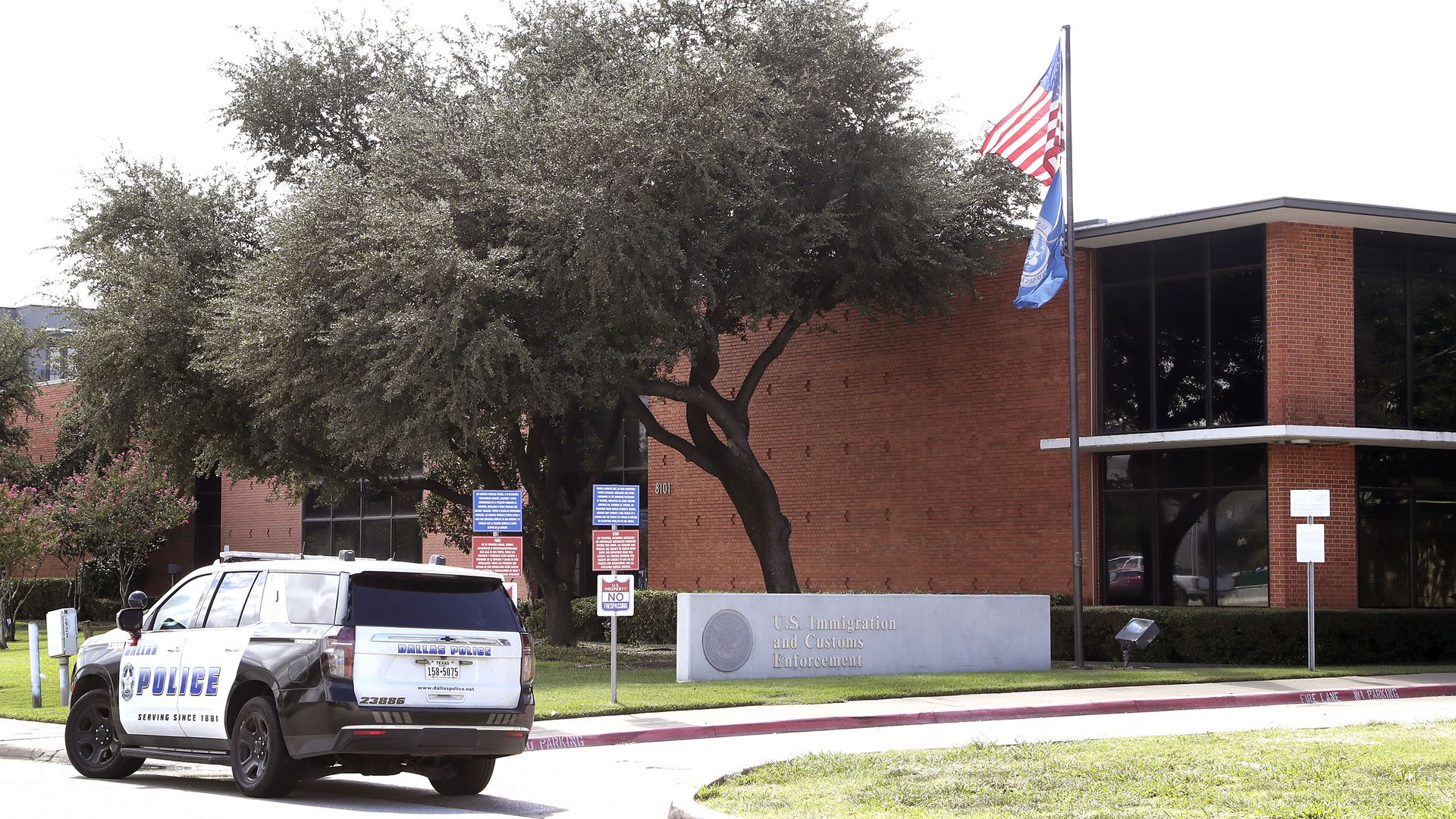 A photo of a Dallas Police Department SUV parked in front of a brick building with a sign out front that says U.S. Immigration and Customs Enforcement 