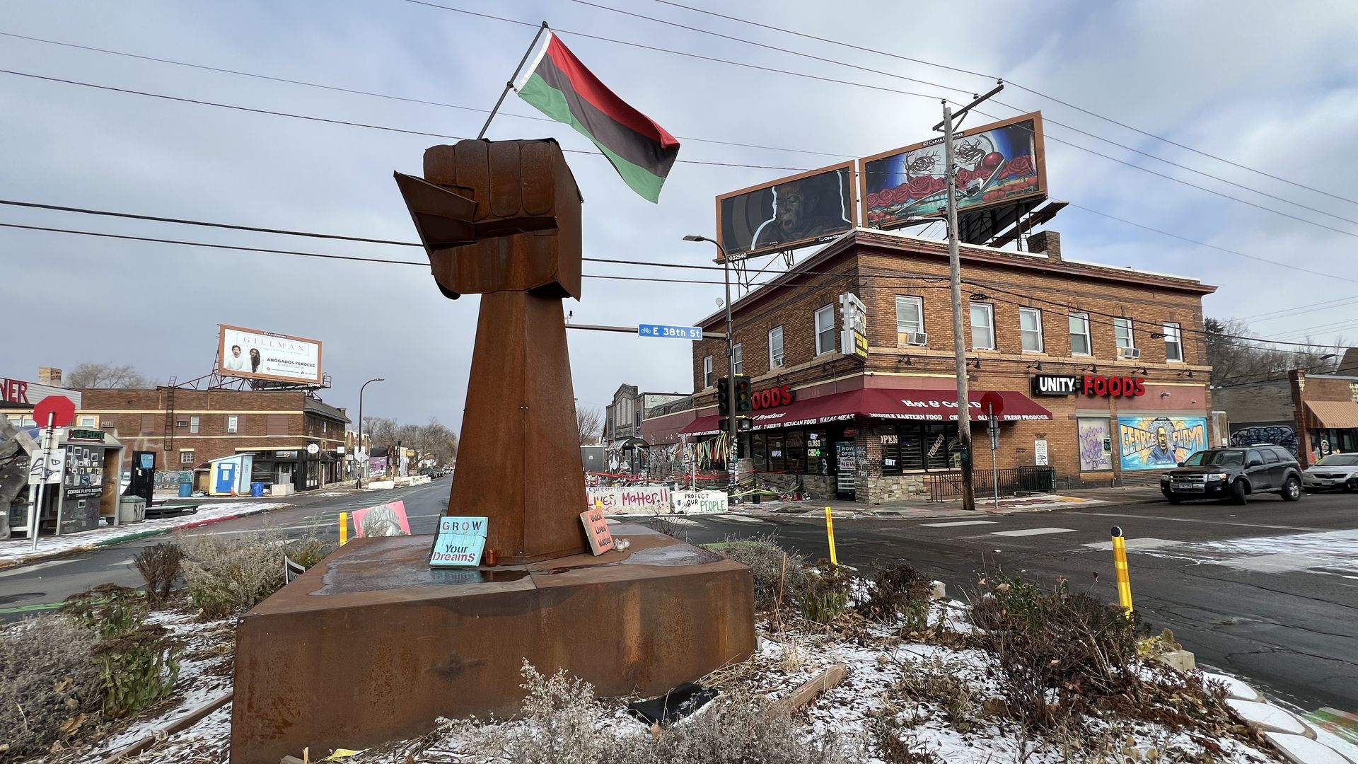 A metal sculpture in the middle of an intersection's traffic circle showing a raised fist in a "Black Power" symbol with a red, black and green Pan-African flag being held out of the top