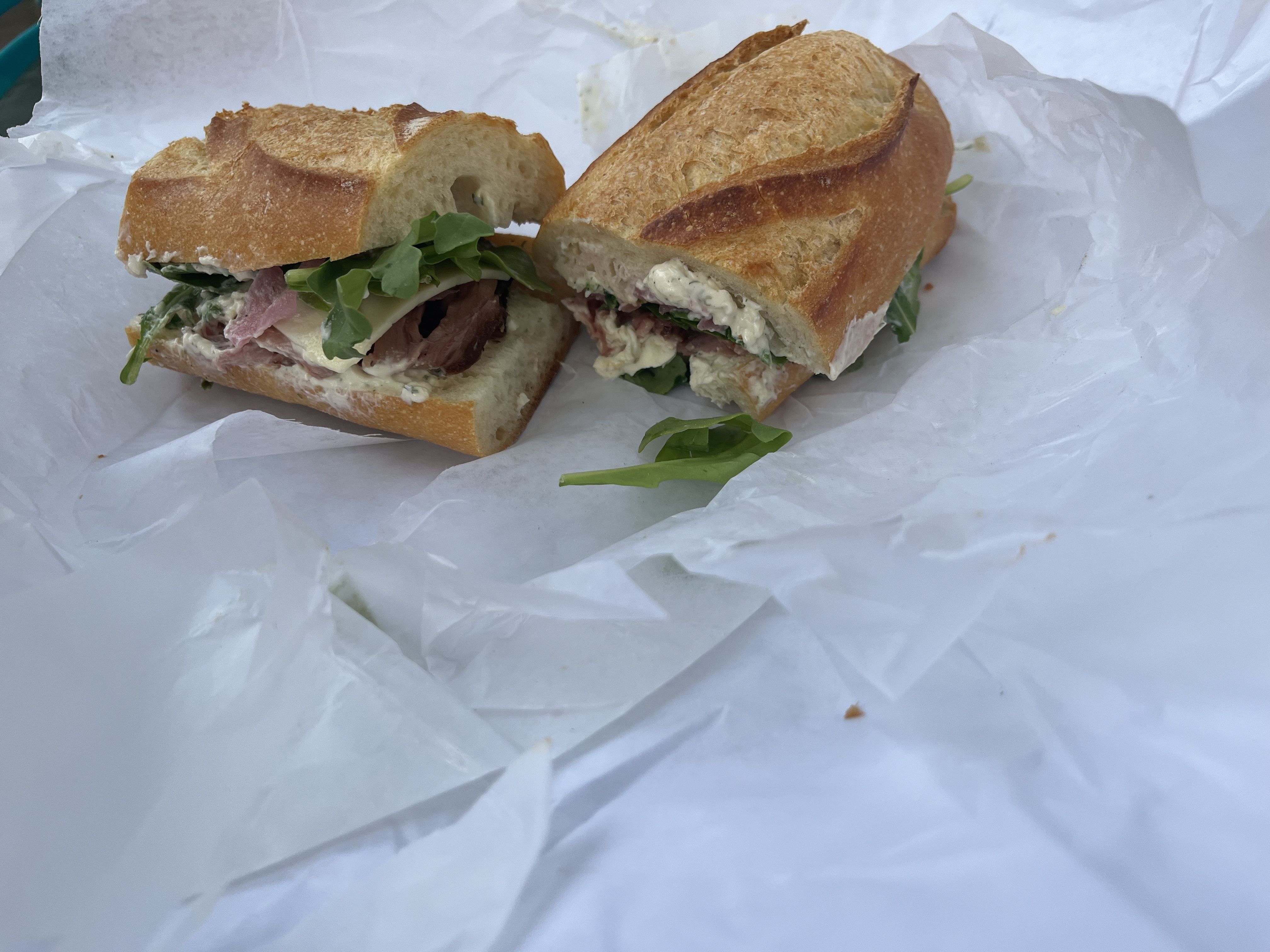 A sandwich on a baguette with roast beef, cheese and arugula coming out 